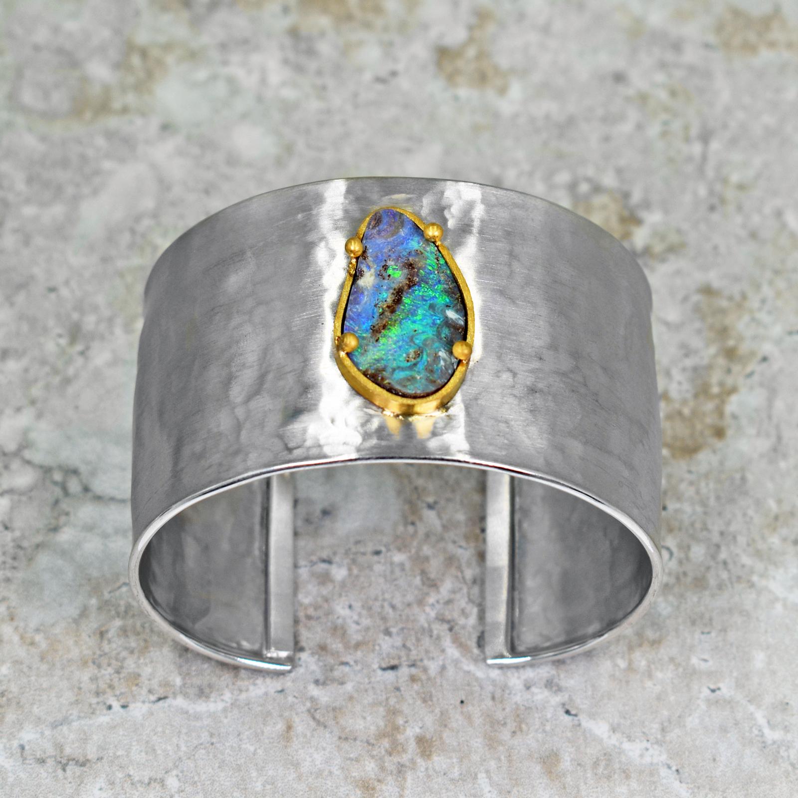 Gorgeous violet and greenish blue Australian Boulder Opal set in 22k yellow gold on a hammered, wide sterling silver cuff bracelet. Silver cuff is 1.5 inches in width. Inside of bracelet is 2.32 inches in width and bracelet opening is 0.94 inches