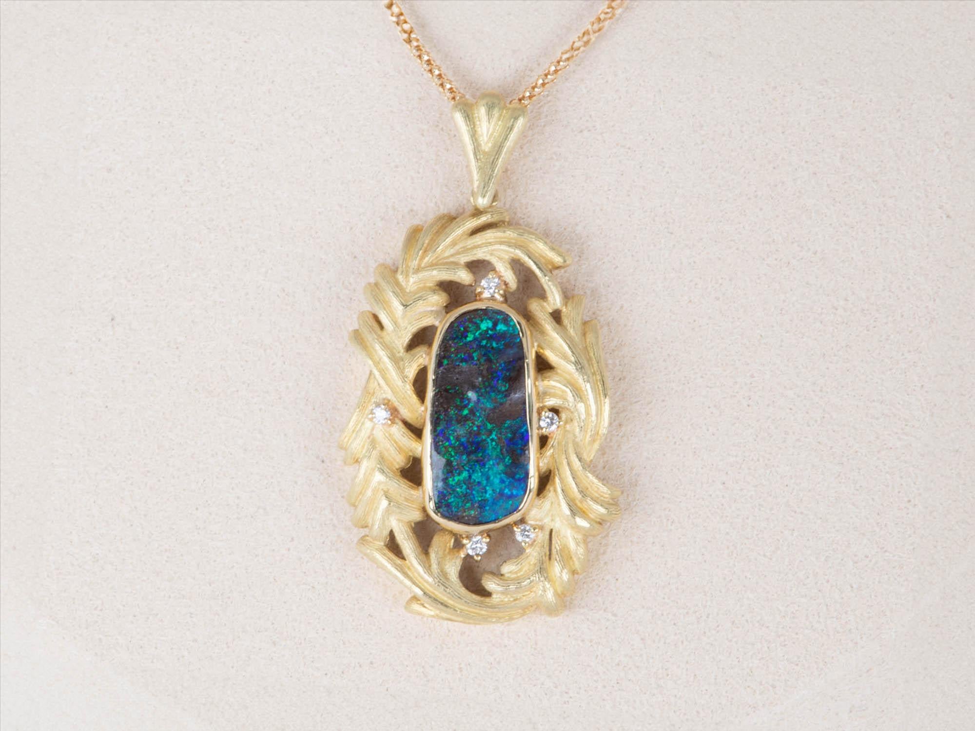 This exquisite Australian Boulder Opal pendant features a stunning feather-like design in a matte texture, crafted in beautiful solid 18K gold. The gorgeous opal emits a mysterious dark blue green color of play, perfectly accentuated by the buttery
