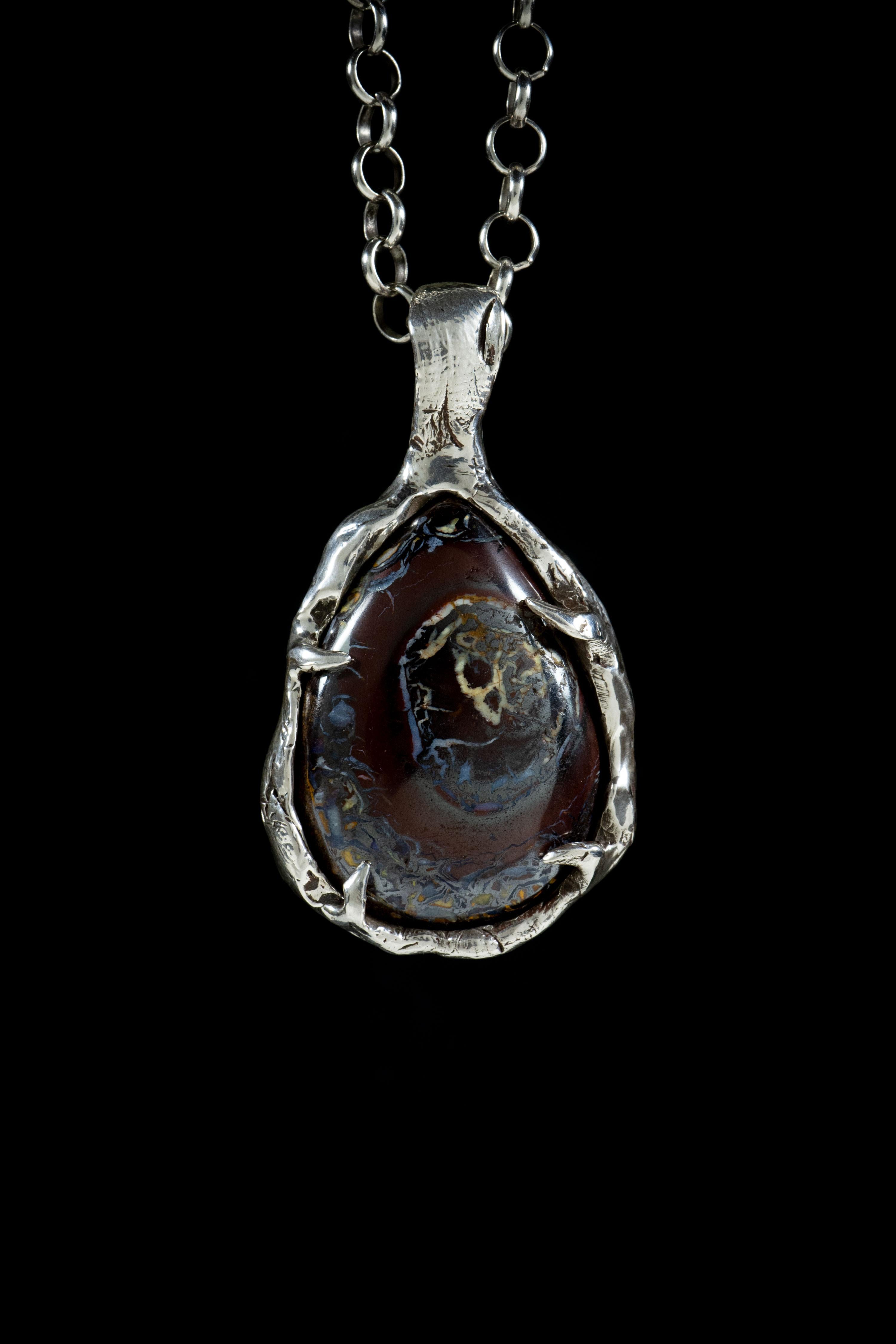 Formation of a Planet is a stunning and unique pendant handcrafted by Ken Fury in sterling silver, featuring a natural Australian Koroit black boulder opal stone. The intricate design of the pendant is inspired by the formation of a planet, with the