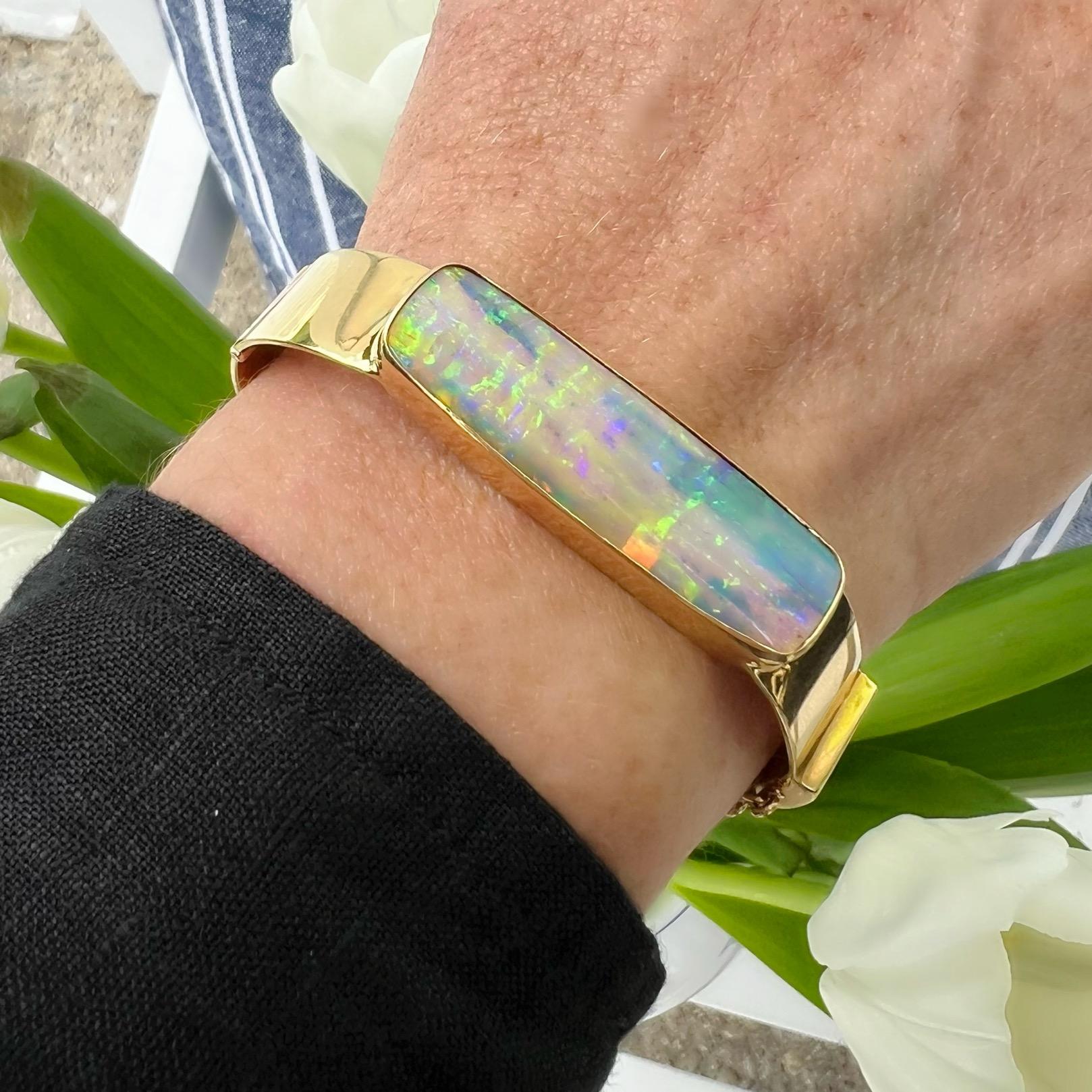 The perfect piece of wrist candy! This 18 karat yellow gold bracelet features an Australian opal weighing approximately 25 carats displaying vibrant light pinks, greens and blues throughout. The bracelet measures 12.5mm at its widest point, weighs