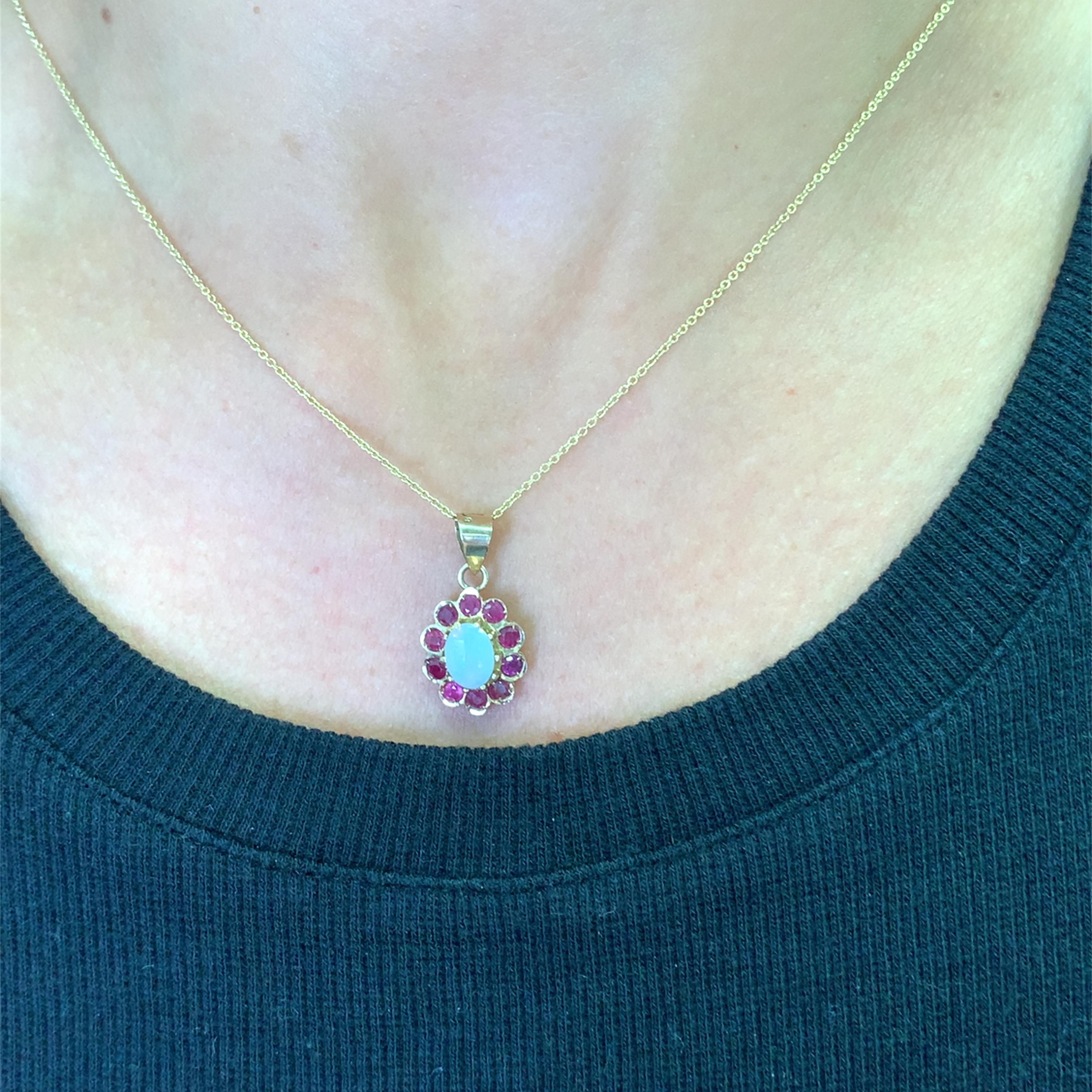 Ornez votre décolleté de ce captivant collier à breloques, orné d'une Opale ovale et d'un ensemble radieux de grenats de forme ronde. Chaque grenat, d'une teinte rouge vif, est soigneusement taillé dans un halo de forme ronde. La monture en or jaune