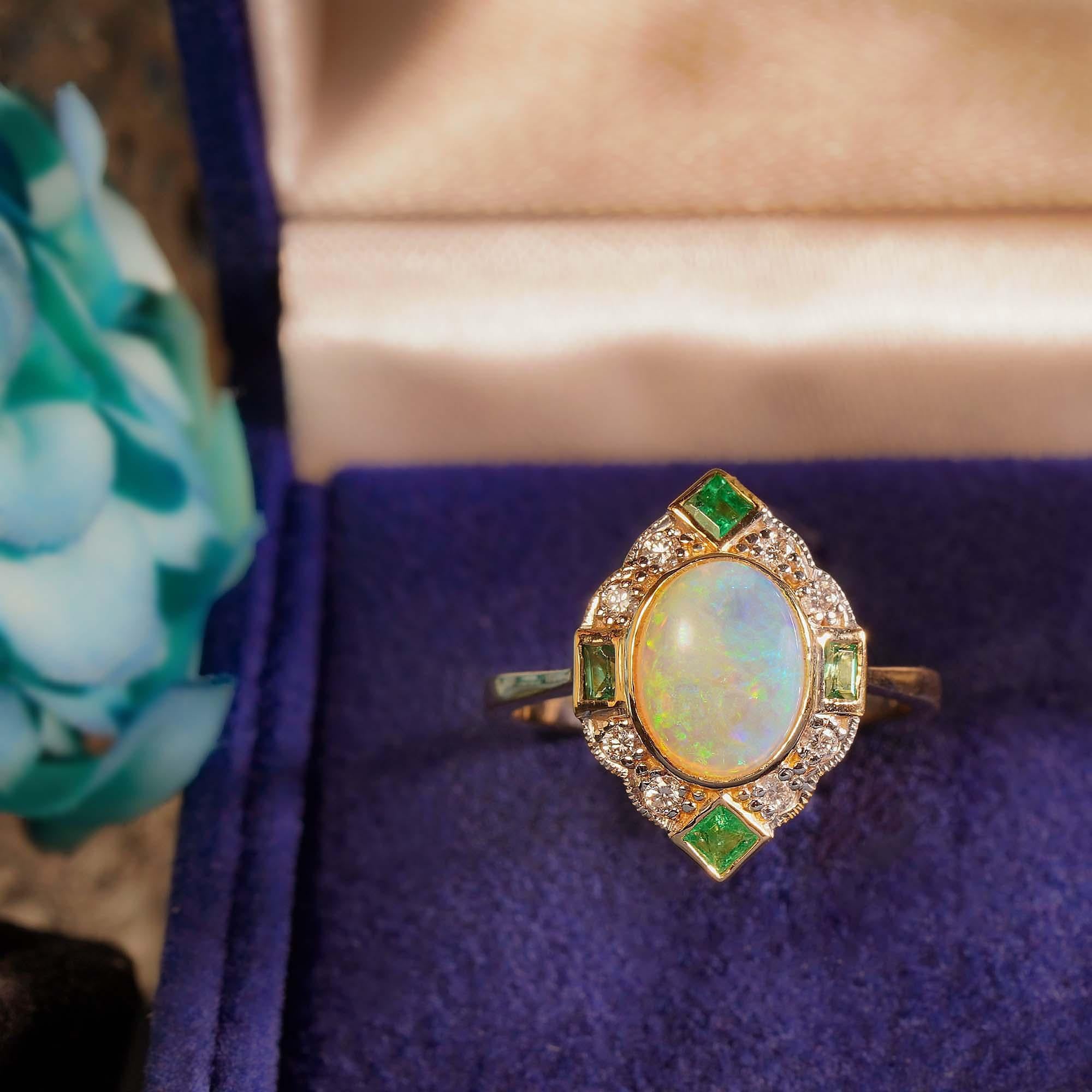 A beautiful natural cabochon Australian opal is bezel set in round diamond halo, punctuated its four with French cut emeralds. The milgrain adds to the vintage style.  

Ring Information
Style: Art-deco
Metal: 14K Yellow Gold (White top diamond
