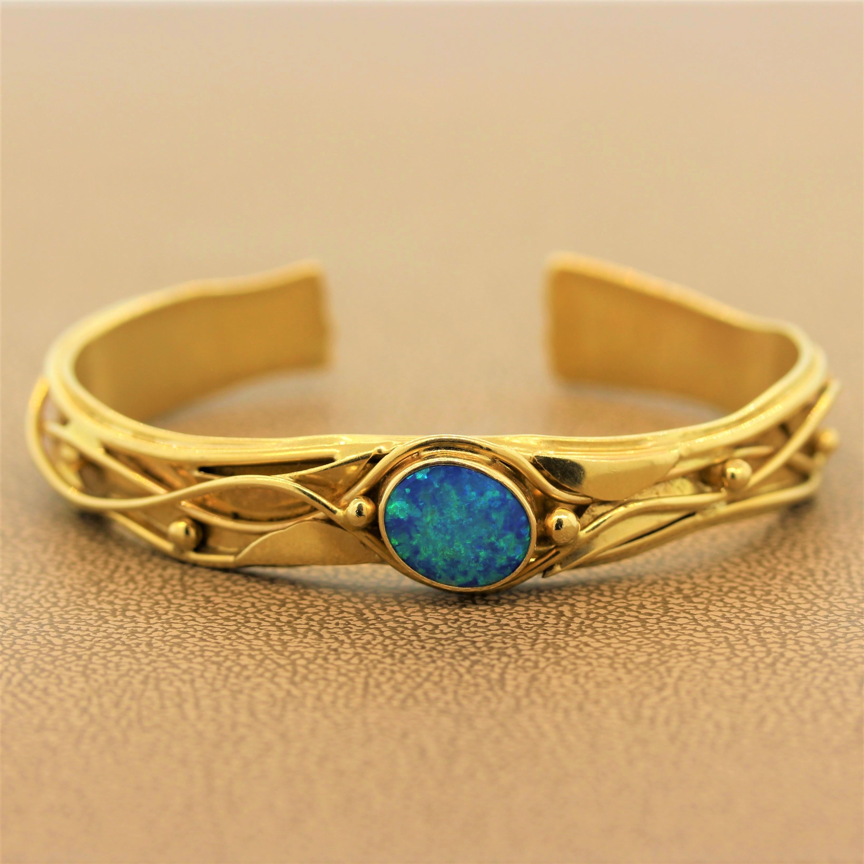 A cuff from designer River featuring a gem Australian opal. The oval shaped opal is bezel set in a 14K yellow gold setting with bead and wavering filigree. The cuff has an opening for easy access for putting on and taking off.  

Cuff Circumference:
