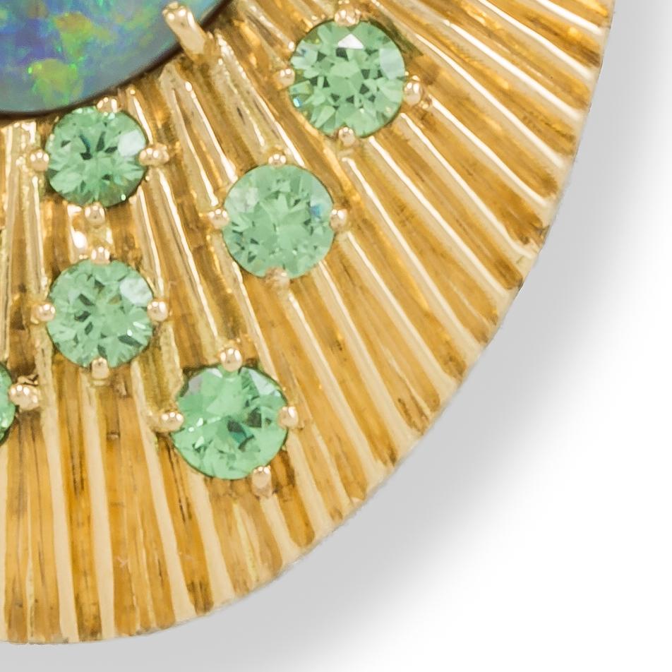 As bright as the rays of the sun the Australian Opal shines out from rich yellow Gold. Garnets sprinkle the golden rays, enhancing the green and blue color play of the Opal. Katherine LeGrand designs and makes her exquisite jewelry at her studio in