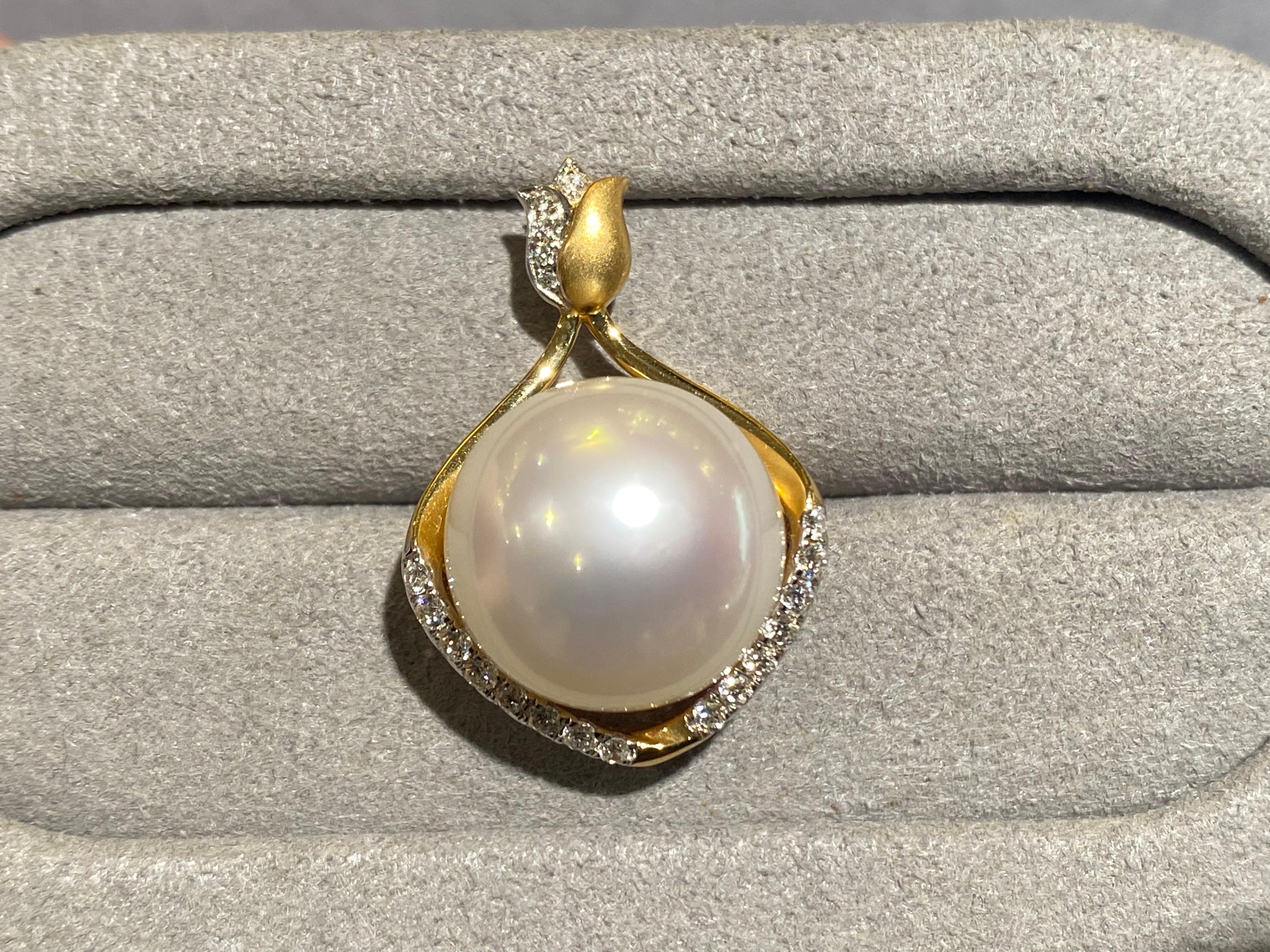A 13.3 mm White Australian South Sea Pearl and diamond pendant in 18k yellow gold. The pearl is set in a rain-drop shape motif with diamond pave at the bottom part of the rain-drop. It has a tulip-like bale set with diamonds. The pearl is white in
