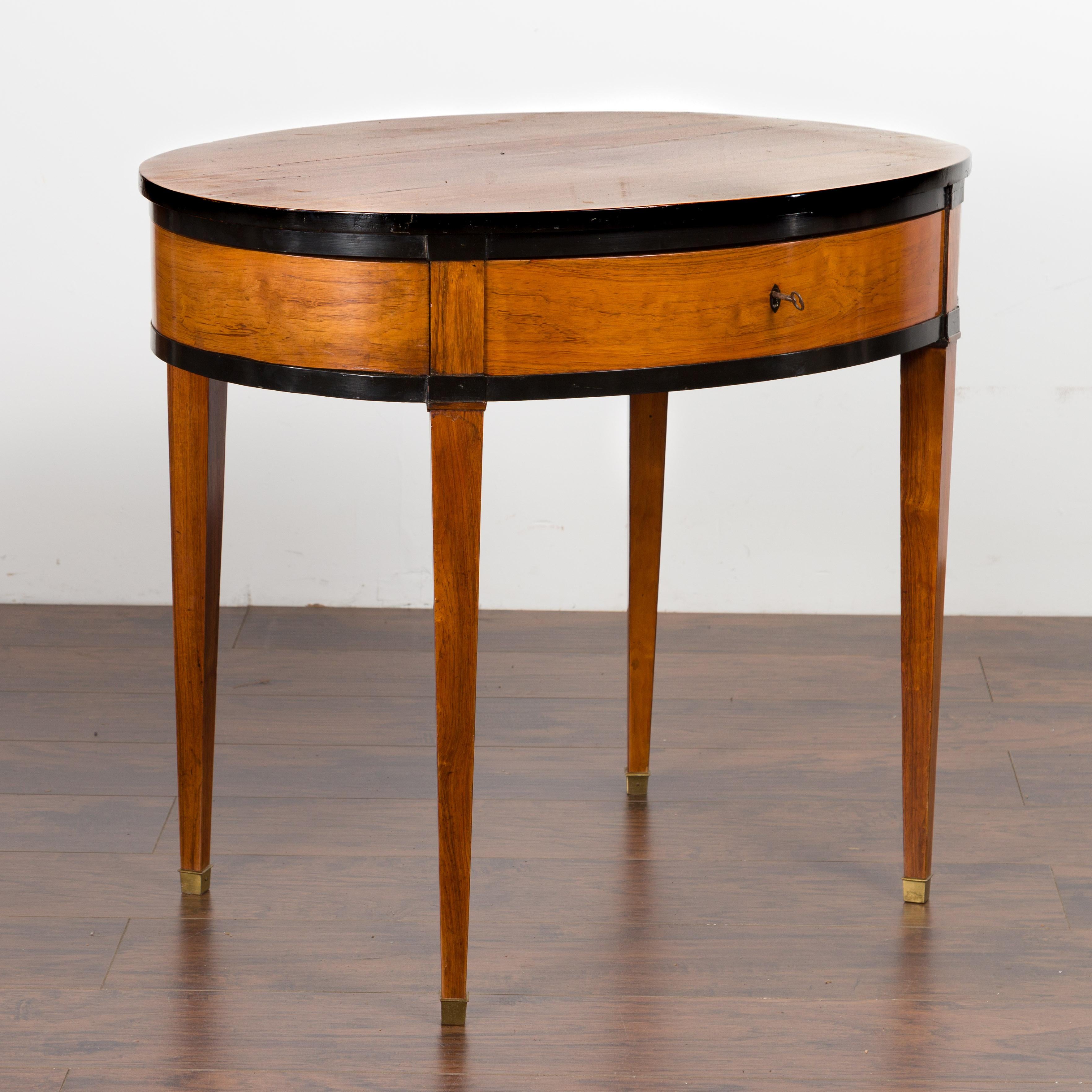 An Austrian Biedermeier period oval top table from the mid-19th century, with ebonized accents and single drawer. Created in Austria during the second quarter of the 19th century, this Biedermeier table features an oval top sitting above a single
