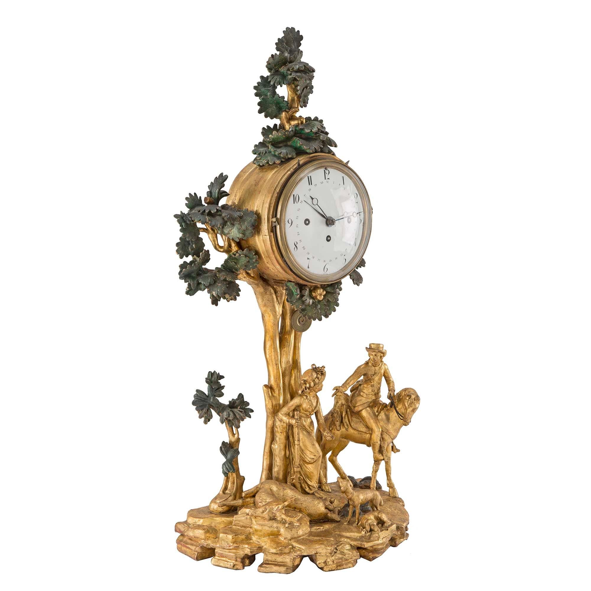 A very unique Austrian 18th century giltwood and polychrome clock, with the original Grand Sonnerie movement. At the base is a country scene of a lady holding a rifle. At her feet are two dogs and a hunters spoils, and a man on a horse beside her. A