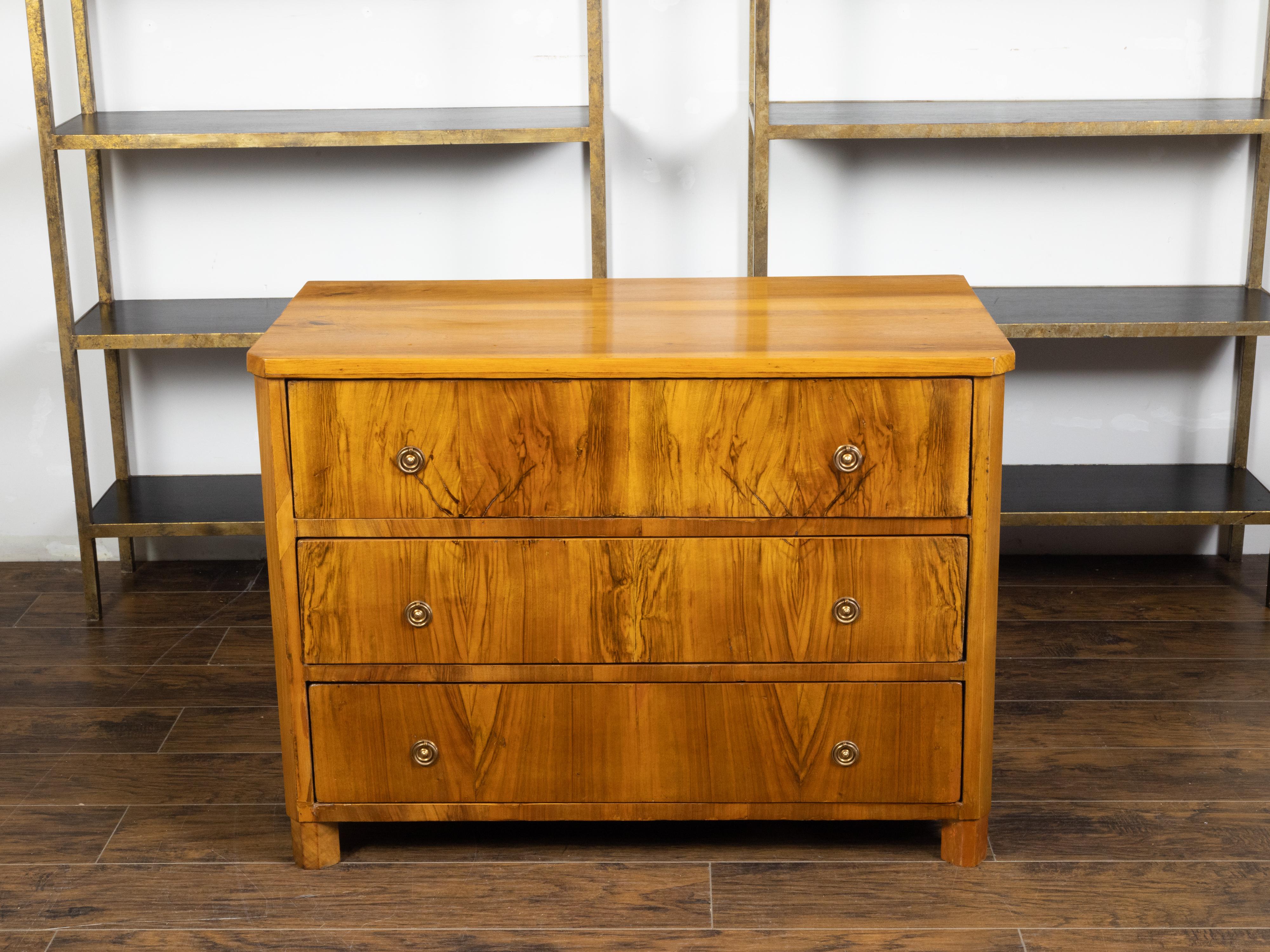 An Austrian Biedermeier commode from the 19th century, with three drawers and block feet. Created in Austria during the 19th century, this Biedermeier commode features a rectangular top with canted corners in the front, sitting above three butterfly