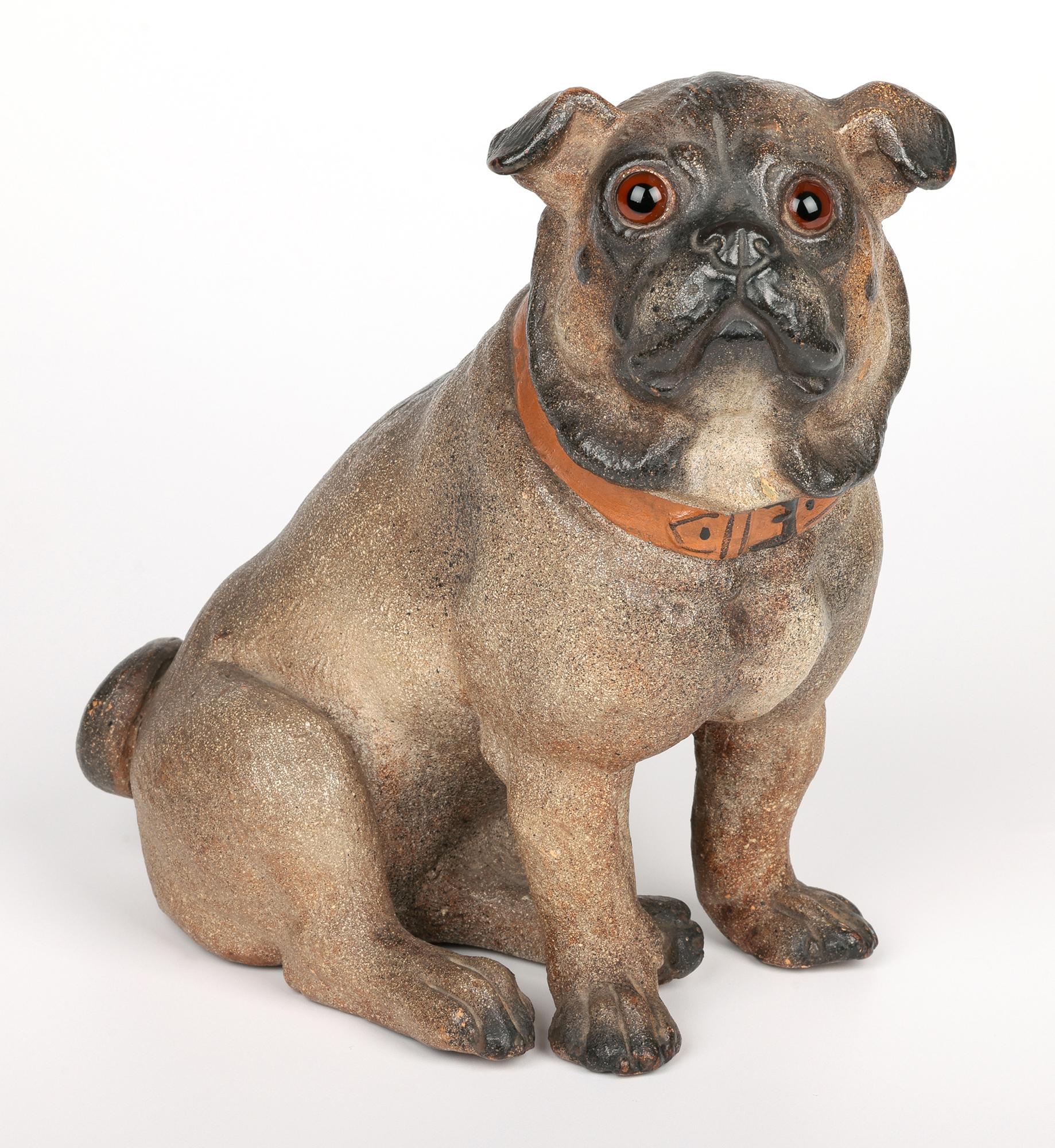 A scarce and stylish antique Austrian art pottery model of a pug dog naturaslistically cold painted and applied with glass eyes and dating from around 1900. The hand modelled terracotta figure portrays the dog seated with its tailed curled and
