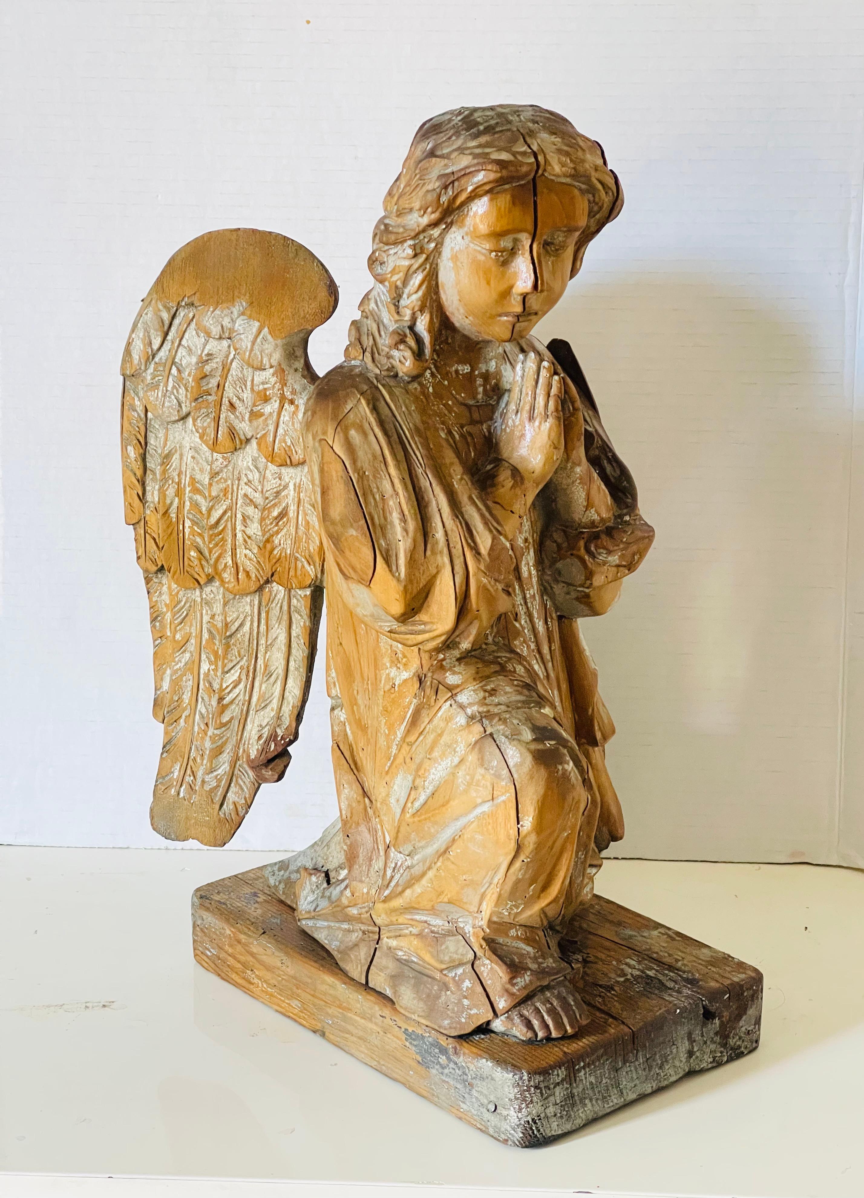 Escultura religiosa austriaca antigua de madera tallada a mano del siglo XIX de un ángel orante, arrodillado sobre. Una rodilla sobre una base de madera. Restos de pintura plateada. Madera partida por la mitad debido al secado de la madera. Hermoso