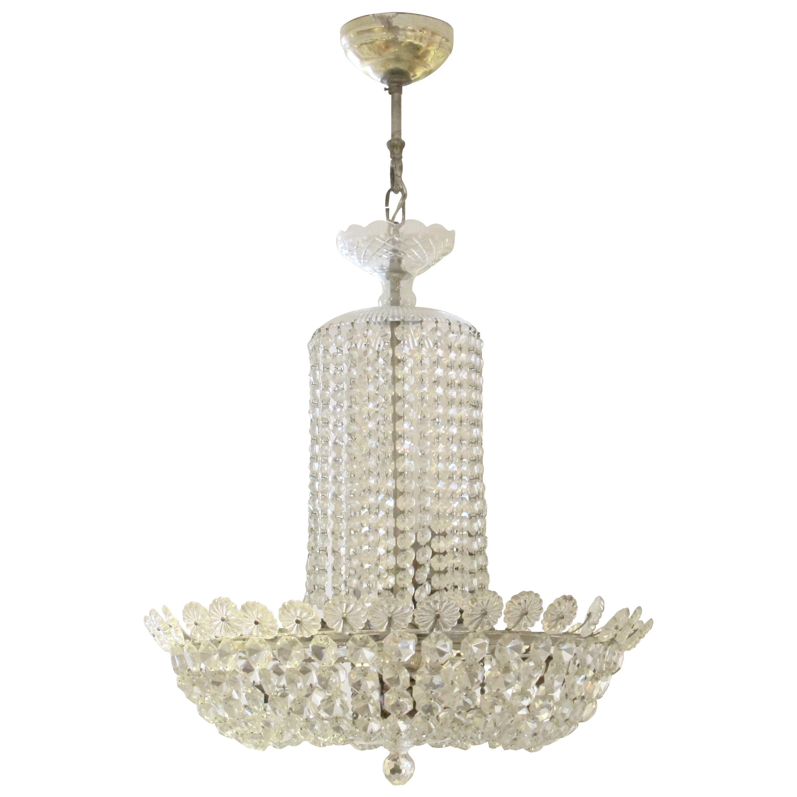 Il lampadario presenta una classica forma a cesto, composta da perle di cristallo sfaccettato finemente tagliate e disposte in graziosi livelli. Una colonna cilindrica di cristallo si riversa in un'ampia coppa svasata, entrambe riccamente ornate da
