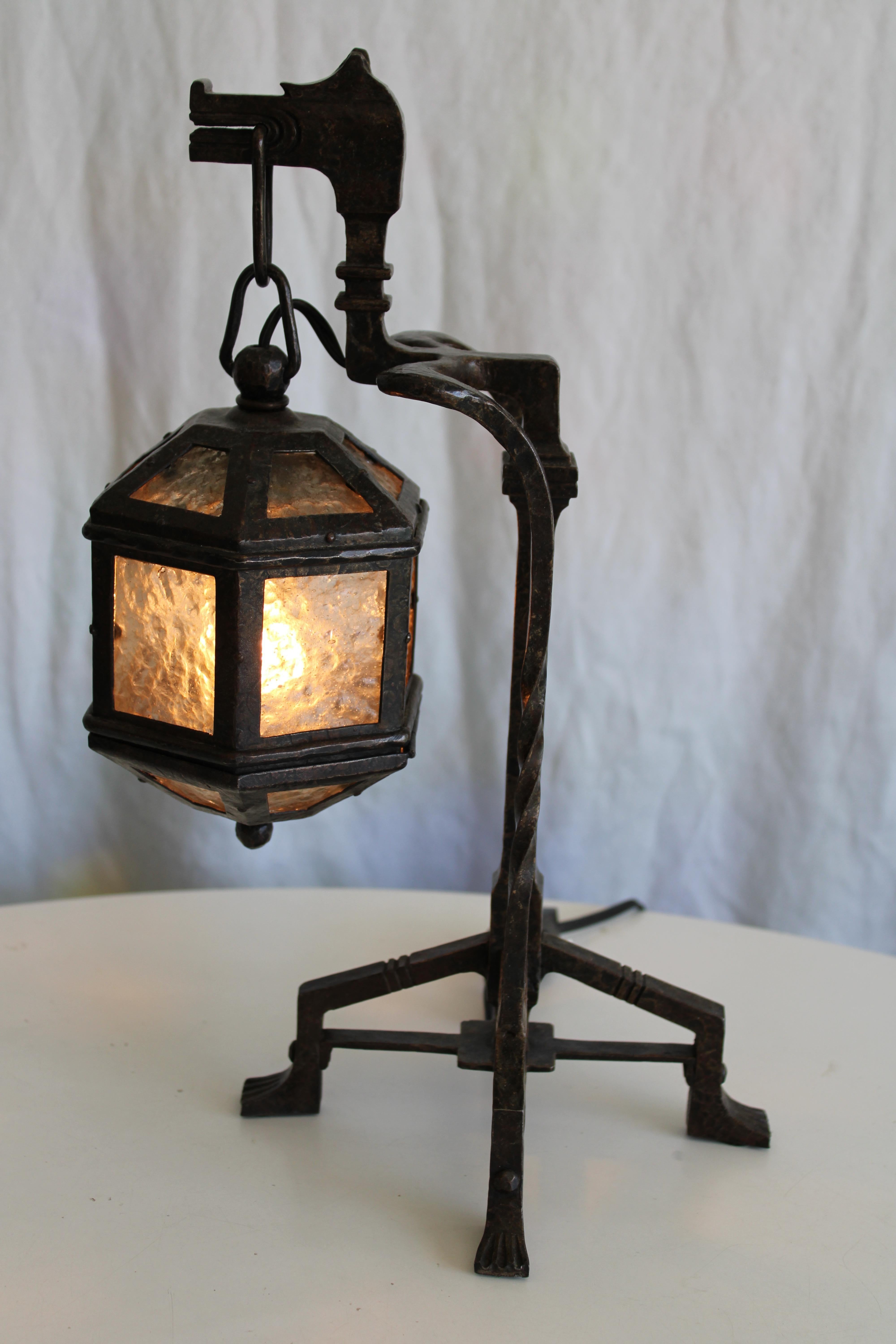 An early twentieth century hand wrought iron table lamp in the abstracted form of a dragon. Lamp is entirely and exquisitely hand crafted. Lantern has eighteen panes of hammered glass, all original. The lamp is 9.5