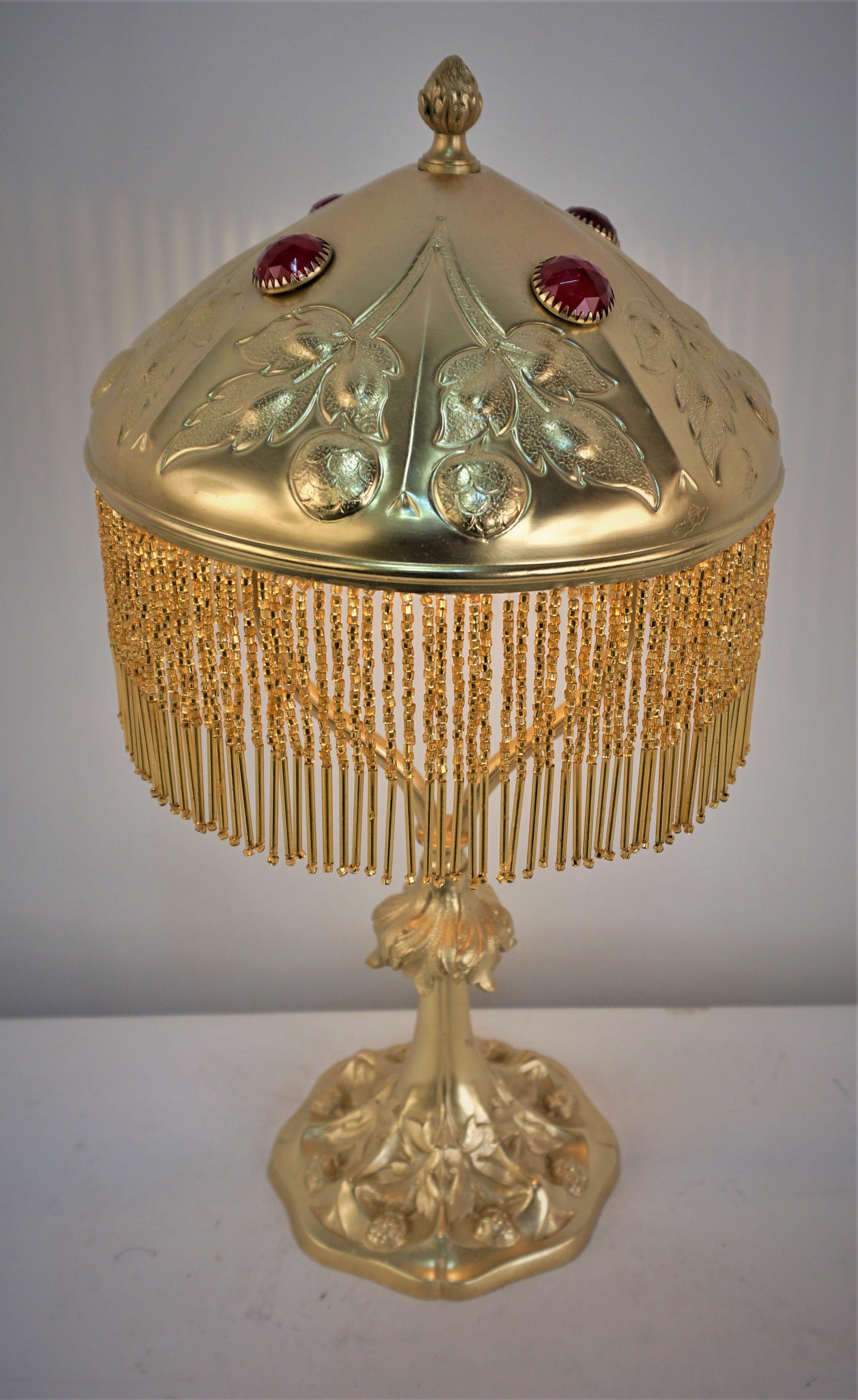 Lampe de table Art Nouveau en bronze avec décor en relief floral et bijou en verre rouge.
