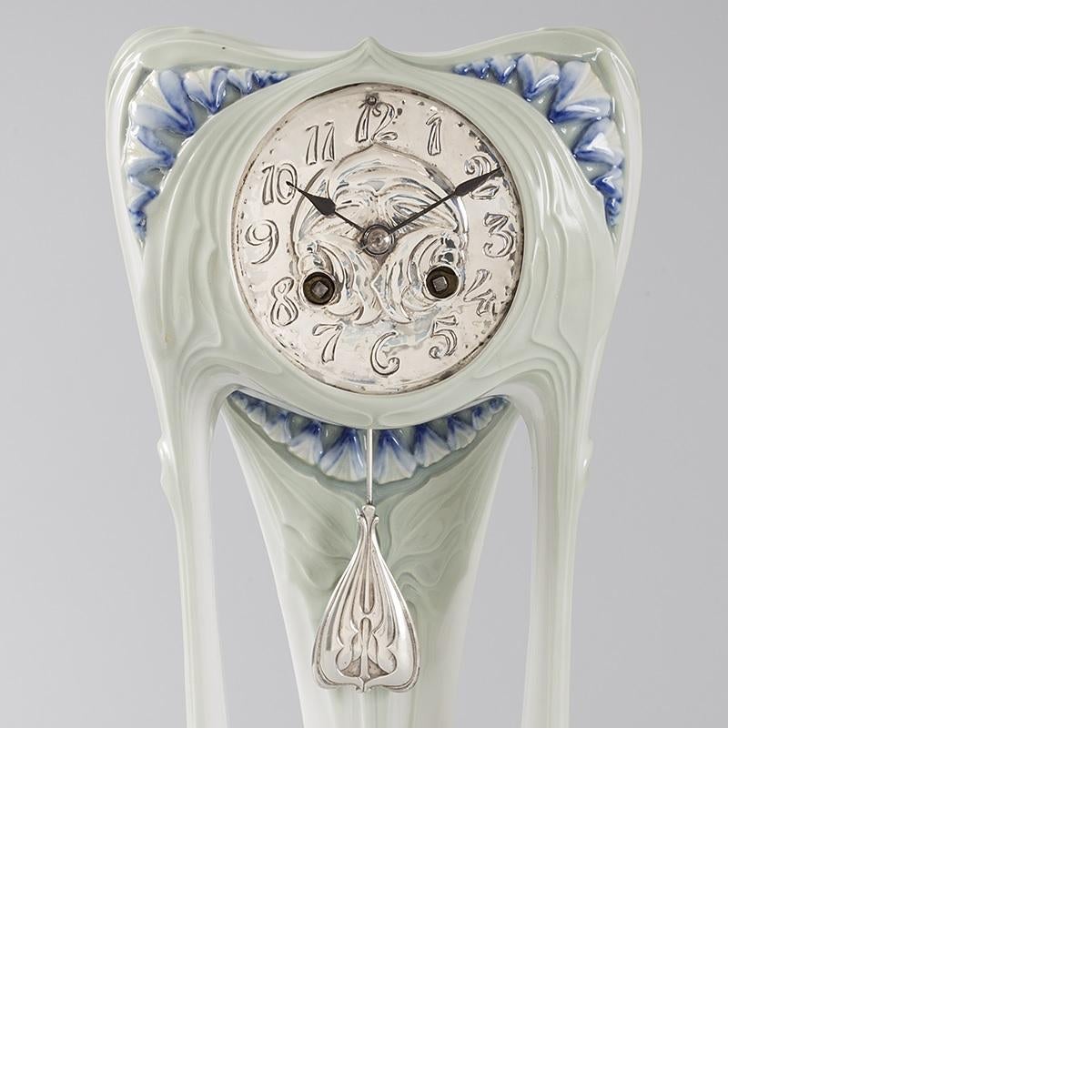 An Austrian Art Nouveau porcelain and silvered clock by Paul Follot. This clock heavily features the arabesquing line of the Art Nouveau movement, both in shape and in the relief decoration. Abstract blue flower buds decorate the clock in panels at