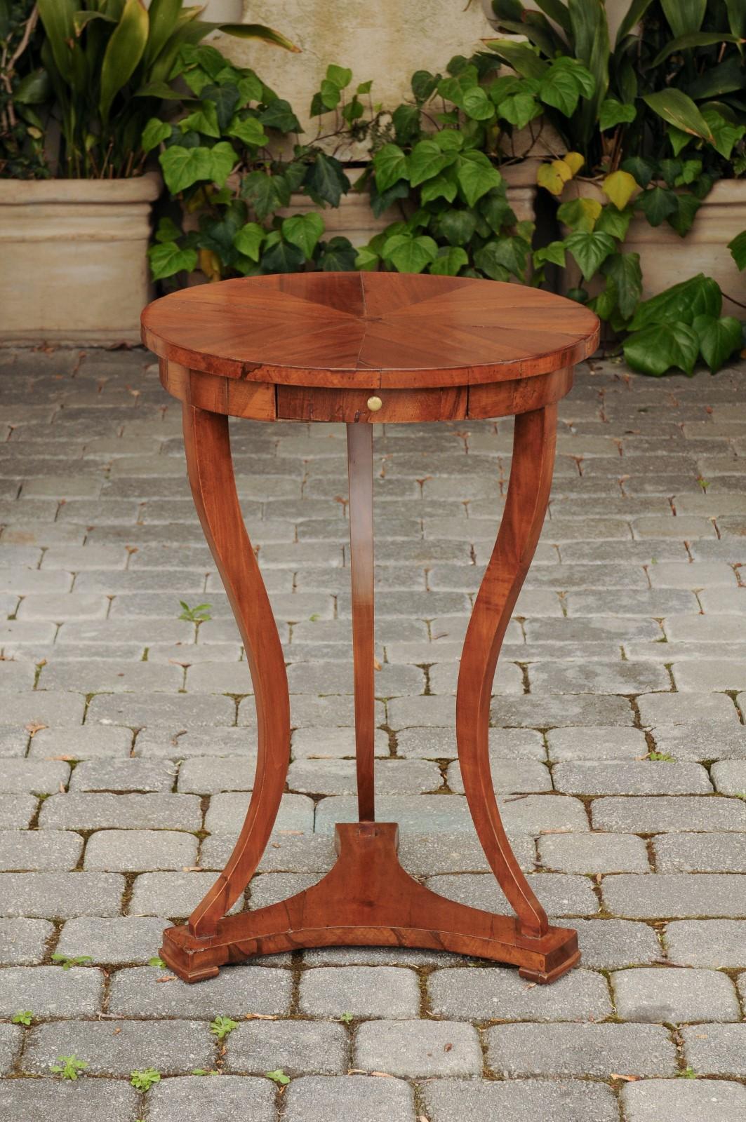 An Austrian Biedermeier period guéridon side table from the mid-19th century, with radiating veneered top, single drawer, cabriole legs and lower shelf. Born in Imperial Austria during the first half of the 19th century, this guéridon features an