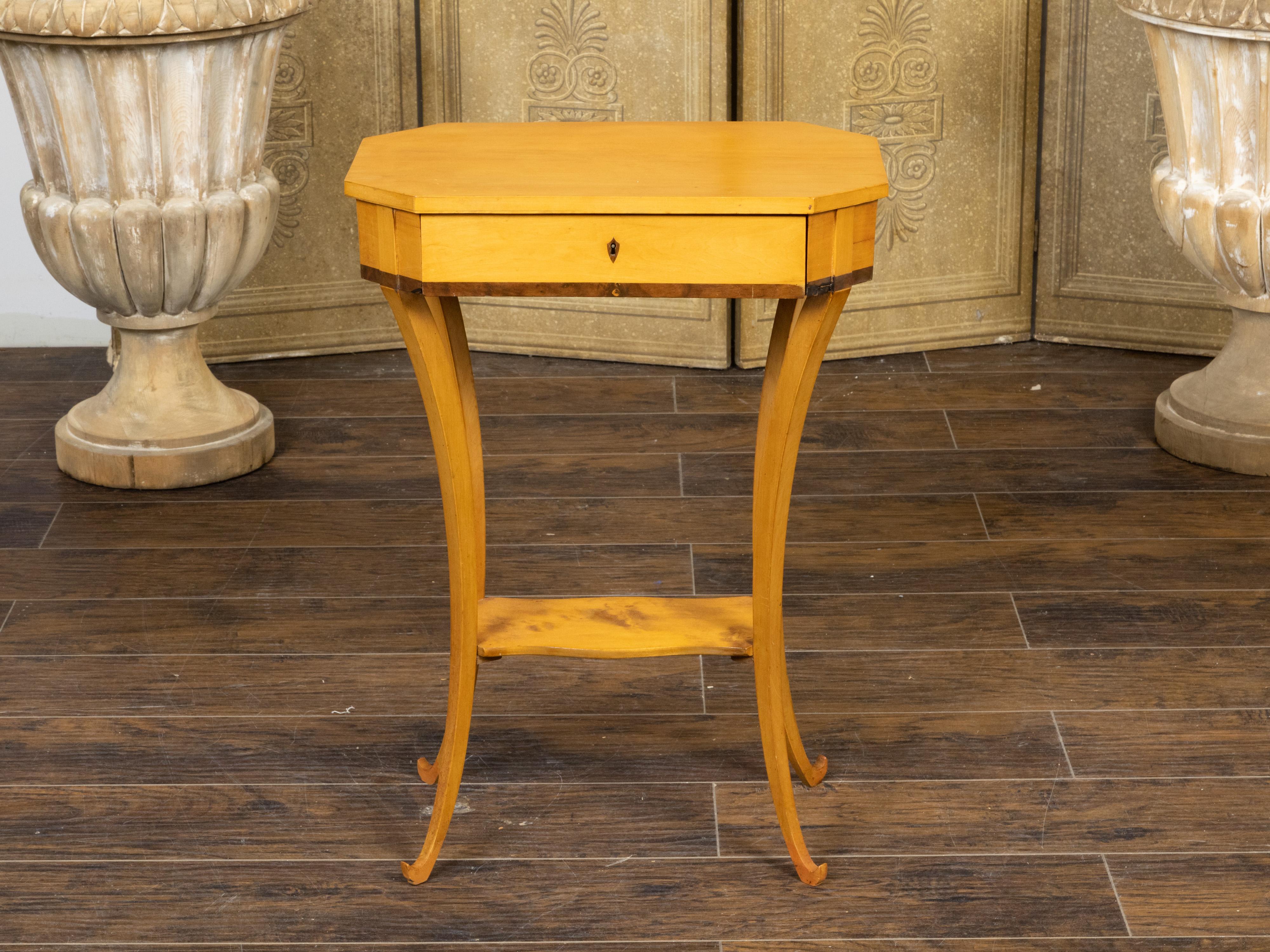 An Austrian Biedermeier period end table from the mid 19th century, with octagonal top, darker accentuation, partitioned drawer, saber legs and lower shelf. Created in Austria during the Biedermeier period in the second quarter of the 19th century,