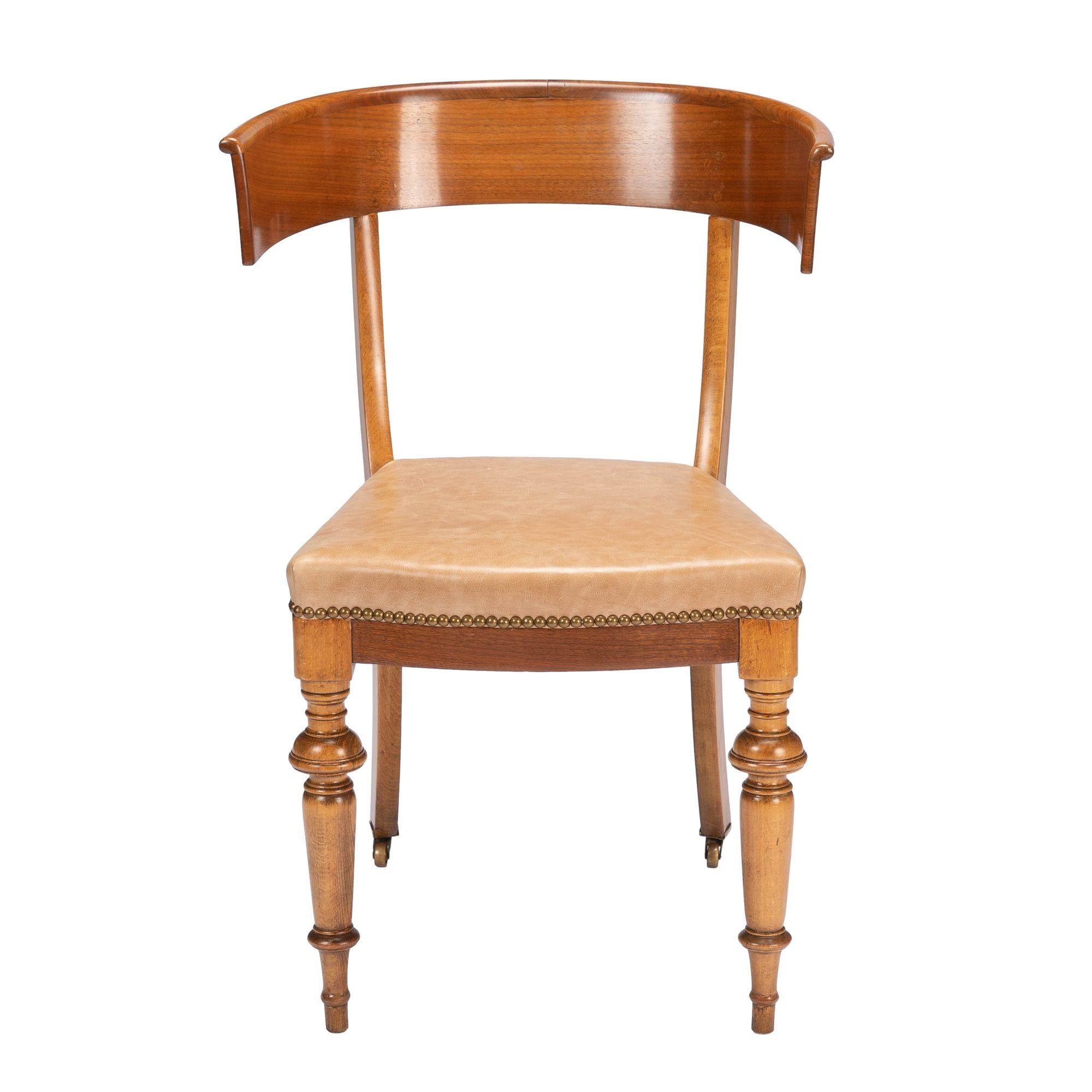 Biedermeier Klismos side chair of European beechwood and mahogany veneers. The seat is upholstered in Italian oil tanned leather with brass round head tacks. The front legs are turned to spike feet and the rear legs are sabre cut on brass castors.