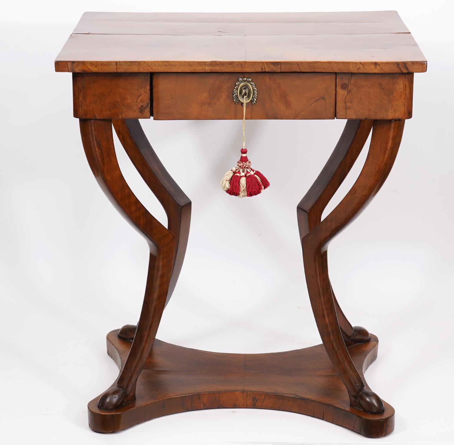 Dating to around 1830-40 This Biedermeier walnut sewing table features sculptural animal style carved legs and stylized hoof feet resting on a shaped base. The drawer is sectioned into paper lined compartments.