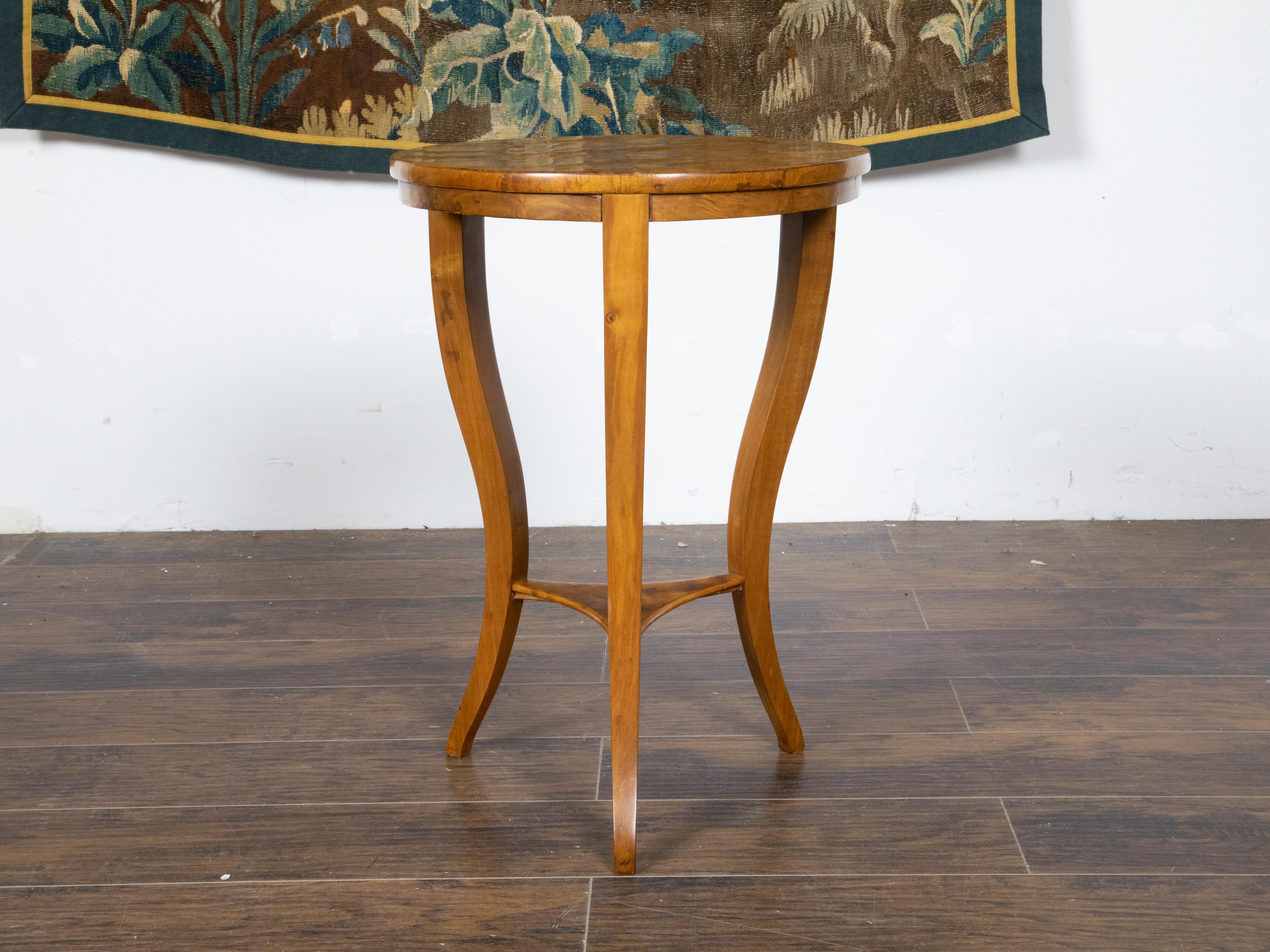 An Austrian Biedermeier period walnut side table from the 19th century with radiating veneer, curving legs and lower shelf. Created in Austria during the Biedermeier period in the 19th century, this walnut side table features a circular top adorned