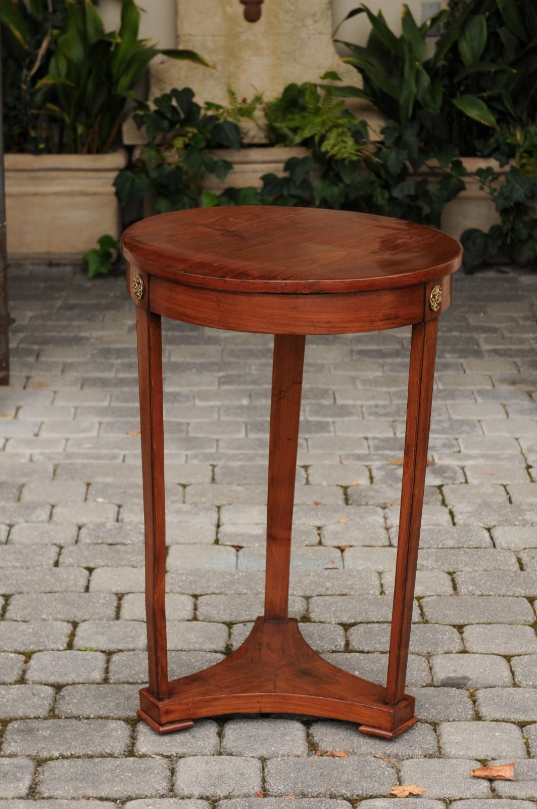 An Austrian Biedermeier period round walnut side table from the first half of the 19th century, with bronze rosettes. This Biedermeier table features a circular top, sitting above an elegant apron, delicately adorned with bronze rosettes