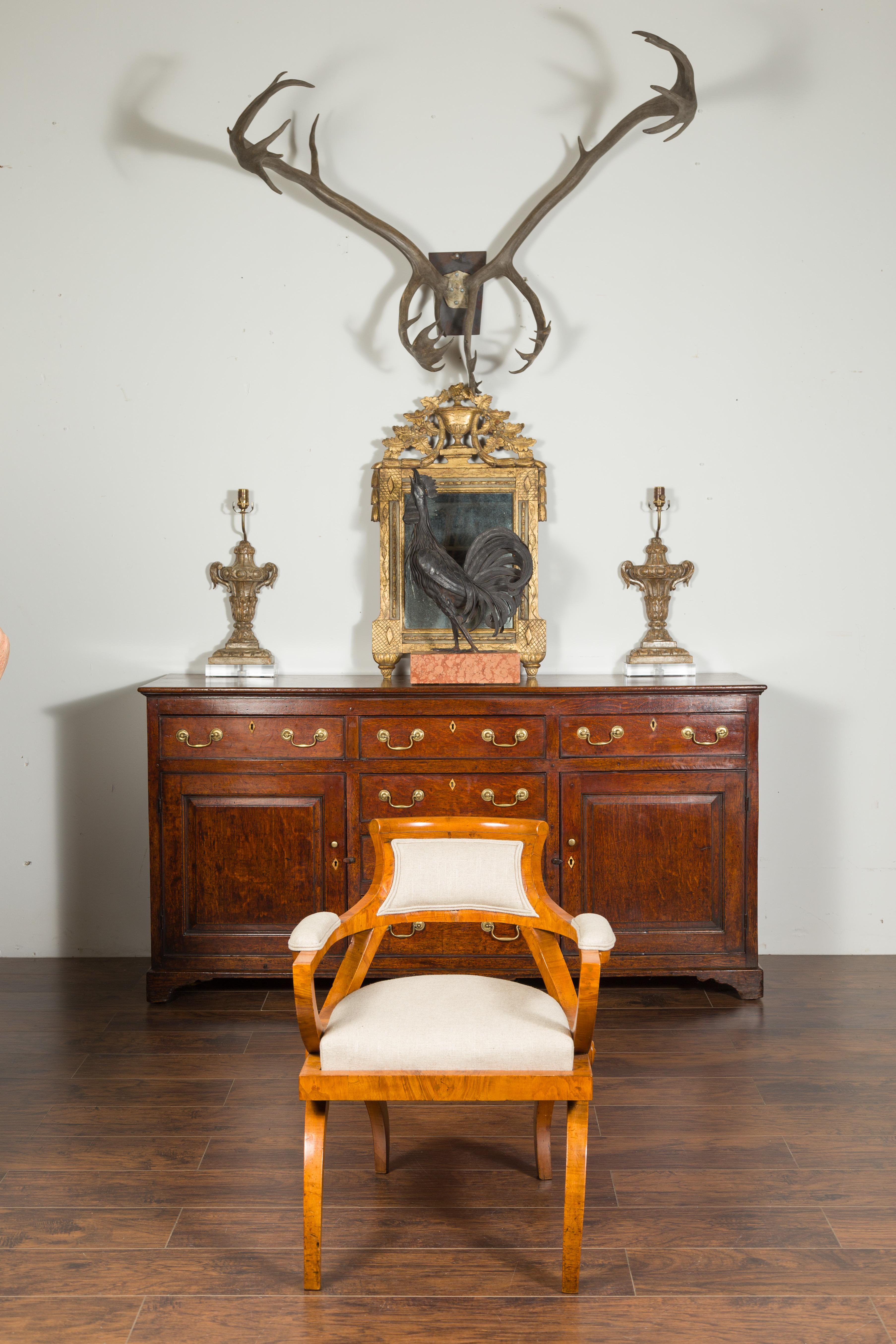 A Biedermeier style walnut veneered armchair from the late 19th century, with arching base and new upholstery. Created in Austria during the third quarter of the 19th century, this Biedermeier style armchair features a small slanted back, flowing