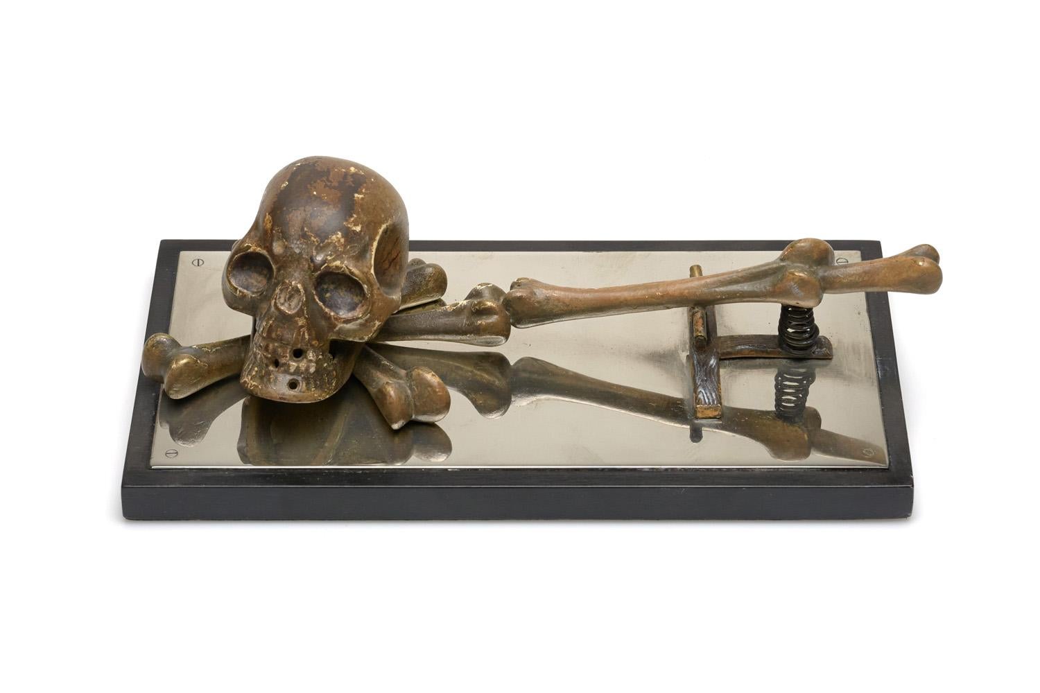 An Austrian bronze desk clip, featuring a large skull and crossbones mounted on wood base with nickel surface.
Early 20th century.
Measures: 8