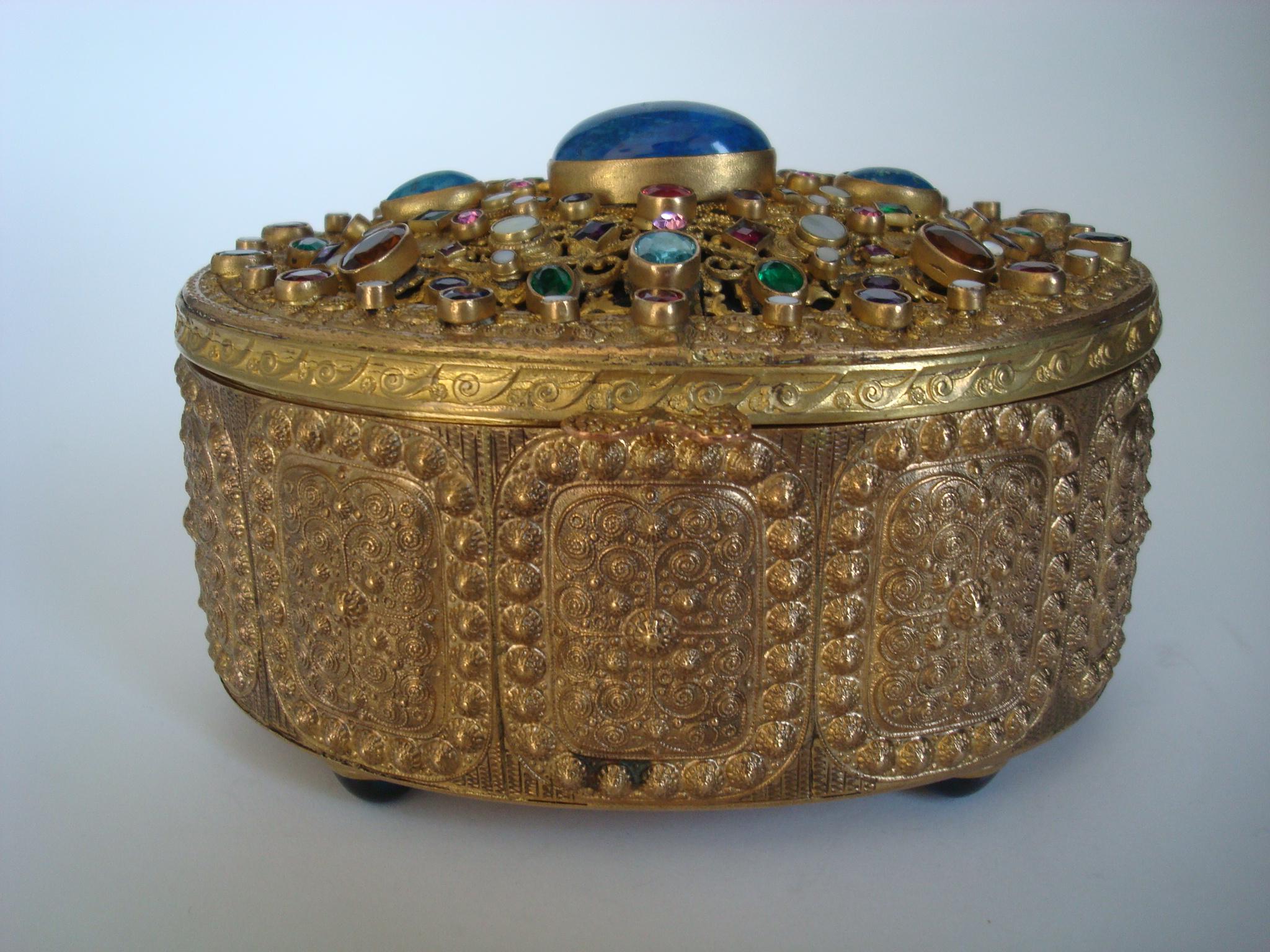 This early 1900s gilded bronze box was made in Austria and shows all the quality of their pieces.
The top has a large central stone. The sides are in an intricate bronze ormolu panel design and the whole box sits on 4 round feet. The interior is