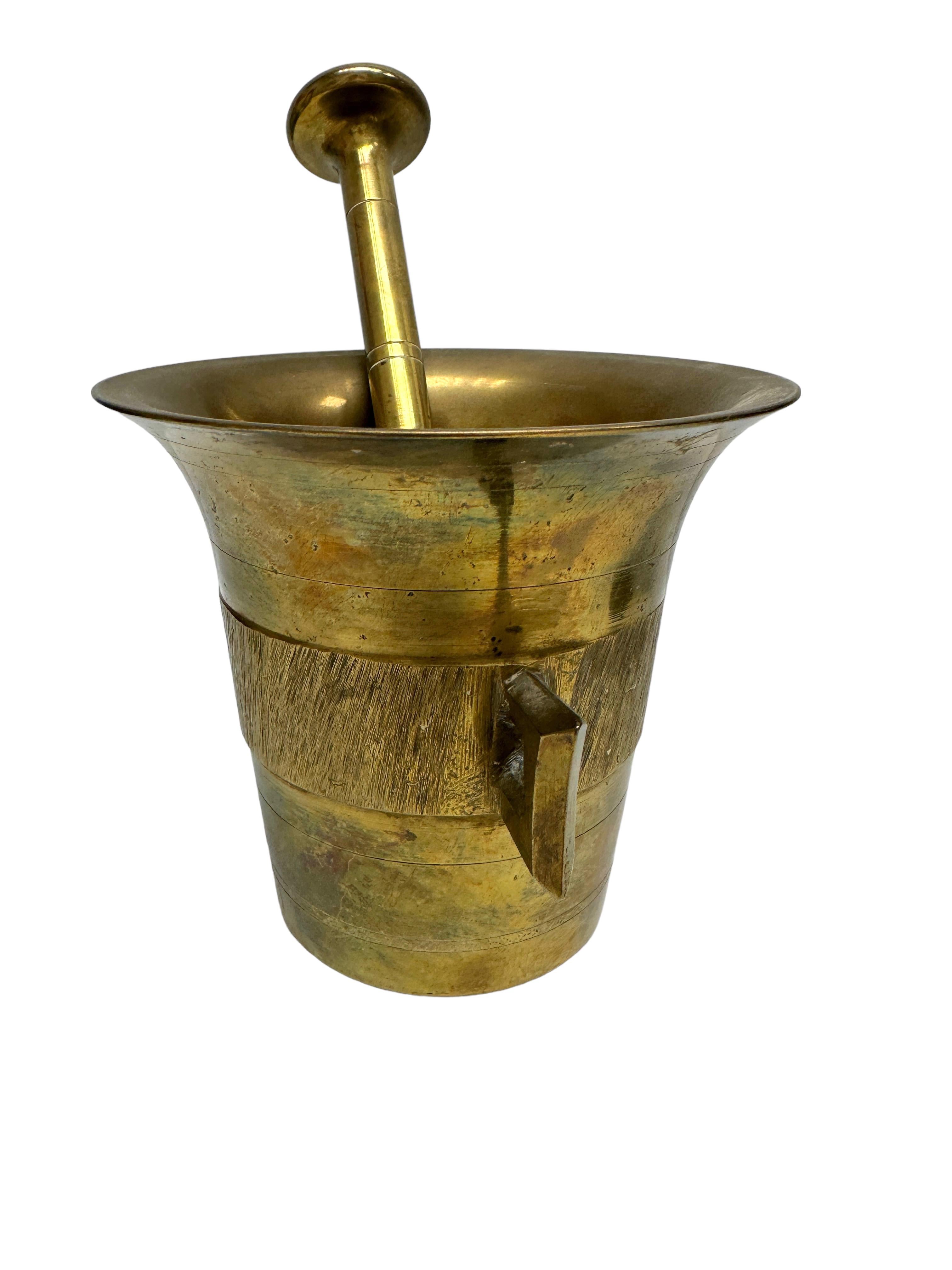 Offered is a beautiful antique solid brass mortar and pestle set. The mortar has a cylindrical shape with a flared mouth and two angular handles at the sides. The baton-shaped pestle has large knob ends at each side to effectively crush and/or grind