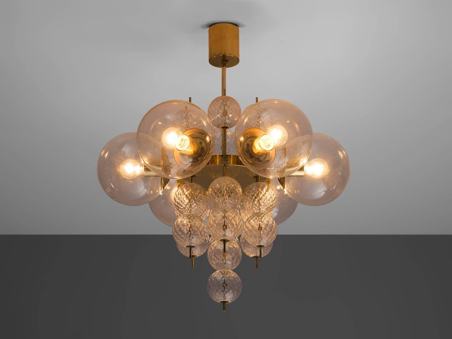 Chandelier, brass, glass, Europe, 1960s.

This exquisite chandelier embodies a brass fixture adorned with art-glass elements. Its circular brass frame contains six lights, each adorned with glass shades. The gentle and ambient illumination it emits