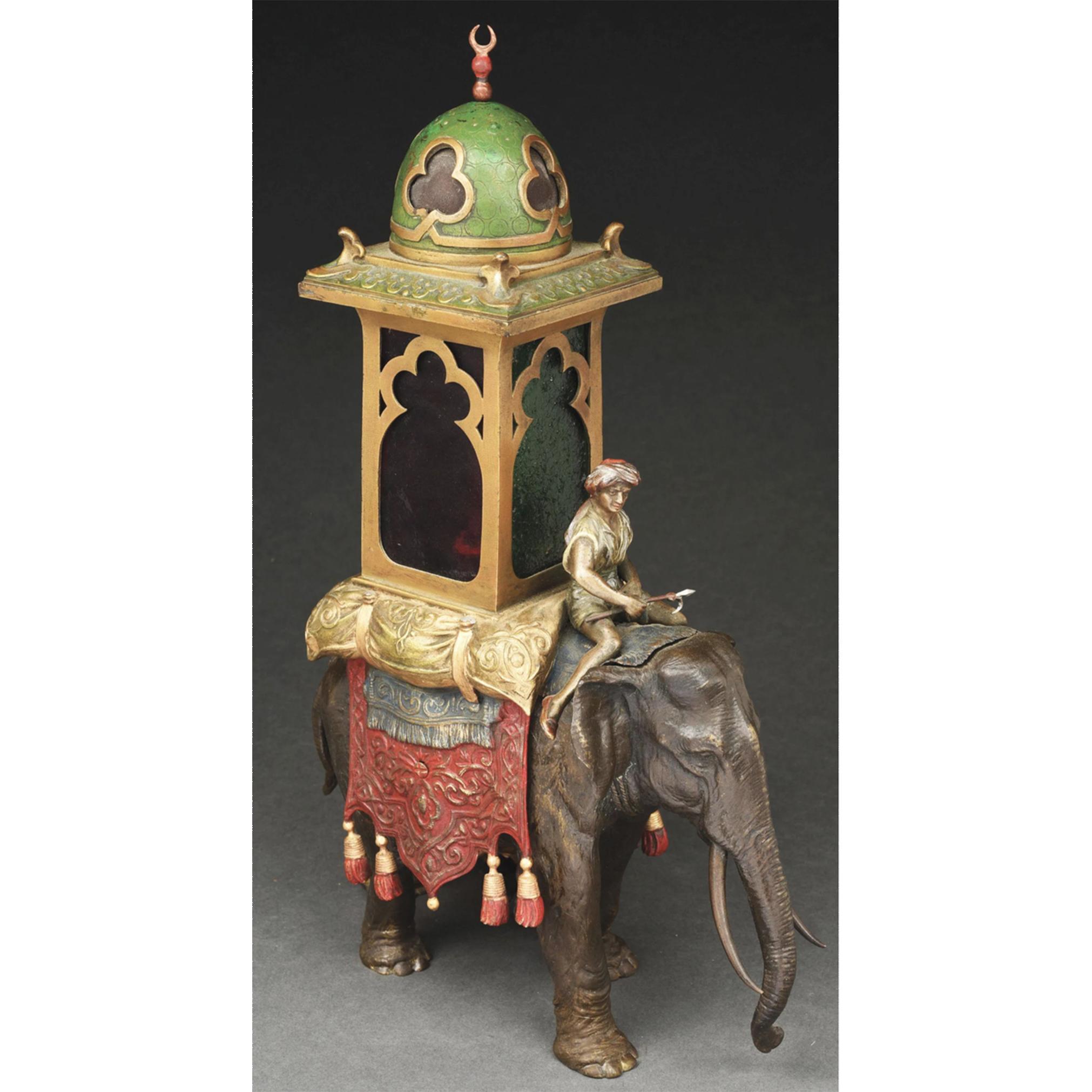 A beautiful Austrian cold painted bronze lamp. The 16” tall lamp with middle eastern motif, feature a large, bronze elephant being ridden by a man, with colorful carpets draped over the elephant. A red and green glass chamber rests atop a gold