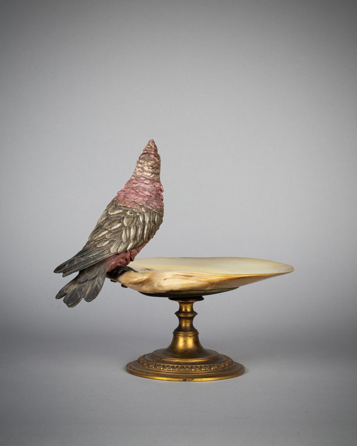 Modell eines Papageis mit rosafarbenen und gelben Federn, der auf einem runden Sockel aus vergoldetem Metall auf dem Rand eines Beckens aus Abalone-Muschel montiert ist.