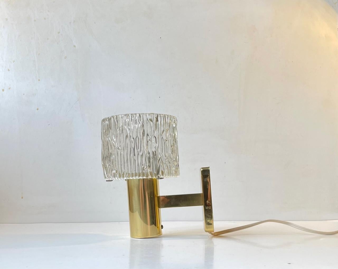 A stylish midcentury Hotel style wall light in gilt brass and textured crystal. Often falsely attributed Hans Agne Jakobsson but actually made by HAGS in Austria during the late 1950s or early 60s. Measurements: H: 19 cm, Diameter: 12 cm, Dept: 17