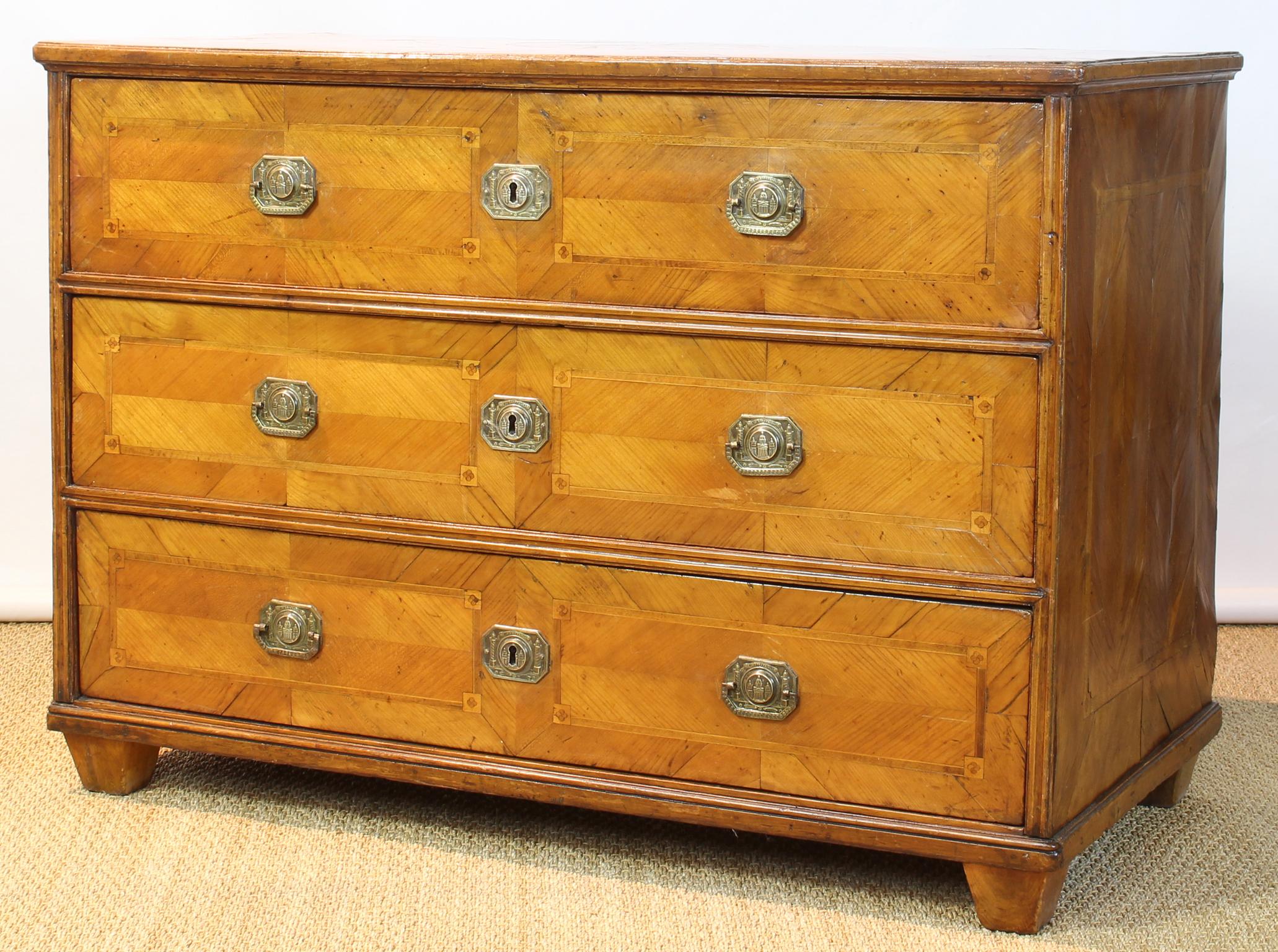 A large and impressive early 19th century. Austrian neoclassical three drawer fruitwood commode with extensive marquetry inlay throughout and original brass pulls in relief depicting the Die St. Karlskirche in Vienna, Austria.