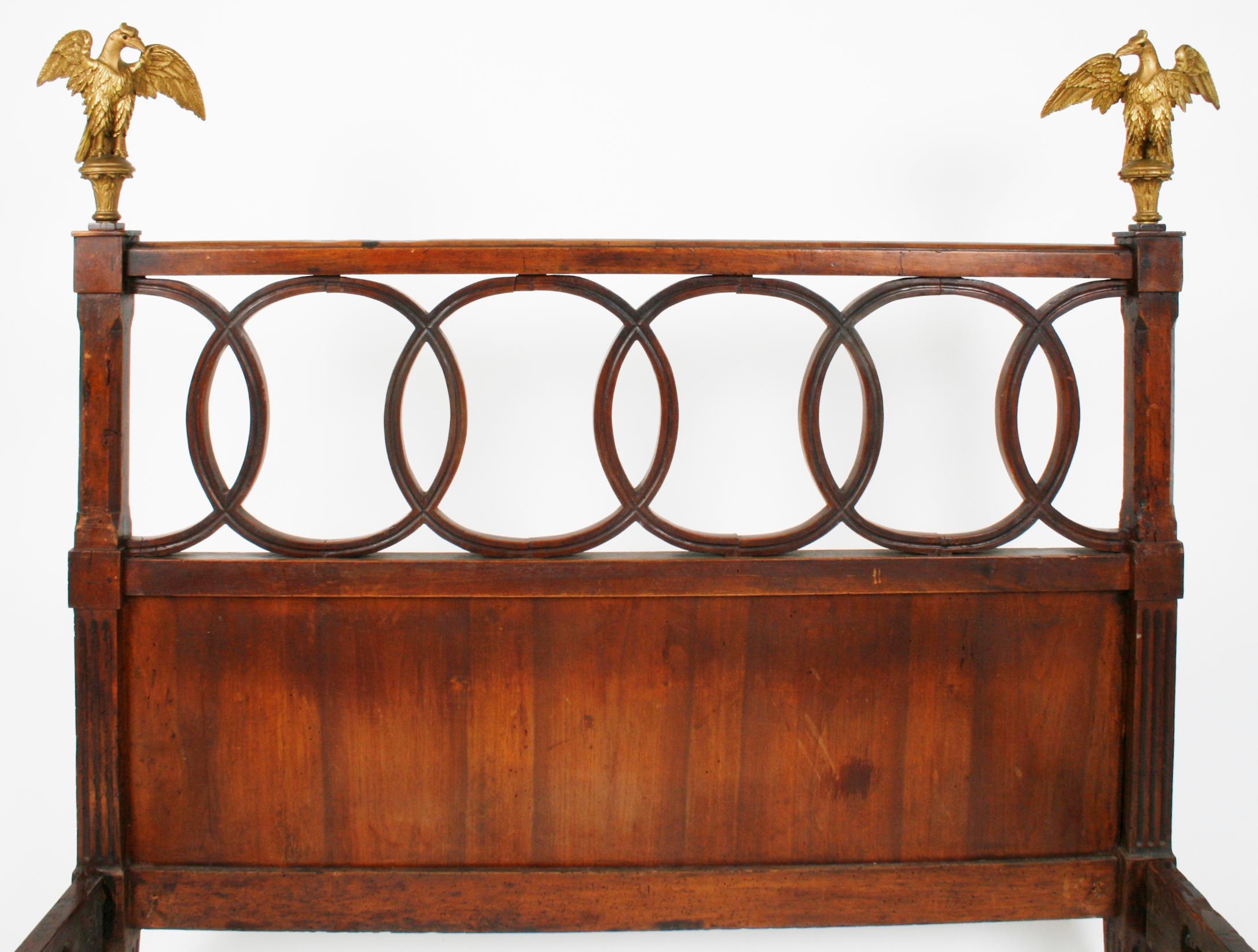 Austrian Empire bed, mahogany, with gilt Habsburg double eagles. The headboard has a framed row of interlocking circles ending at square carved and ribbed posts topped with original gilt carved eagles. It stands on four square ribbed legs. Inside