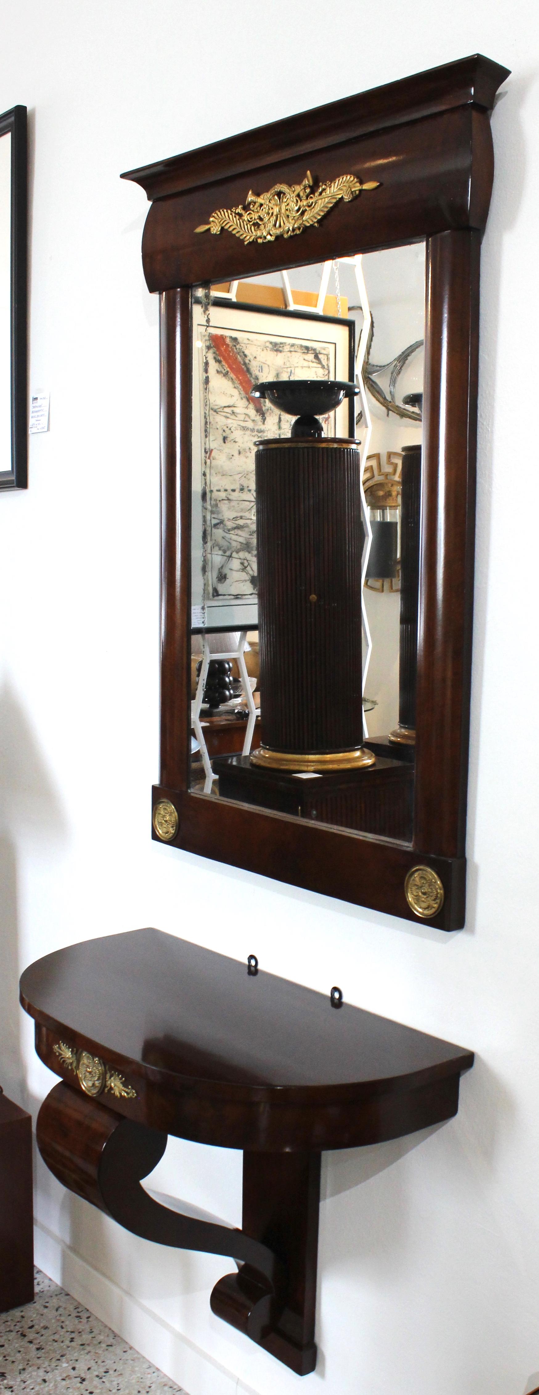 Diese stilvolle wandhängende Konsole im Empire-Stil und der Spiegel stammen aus dem 19. Jahrhundert und wurden in Österreich erworben. Das Stück ist aus Mahagoni gefertigt und mit Bronzedoré-Beschlägen versehen.

Hinweis: Das Stück behält seinen