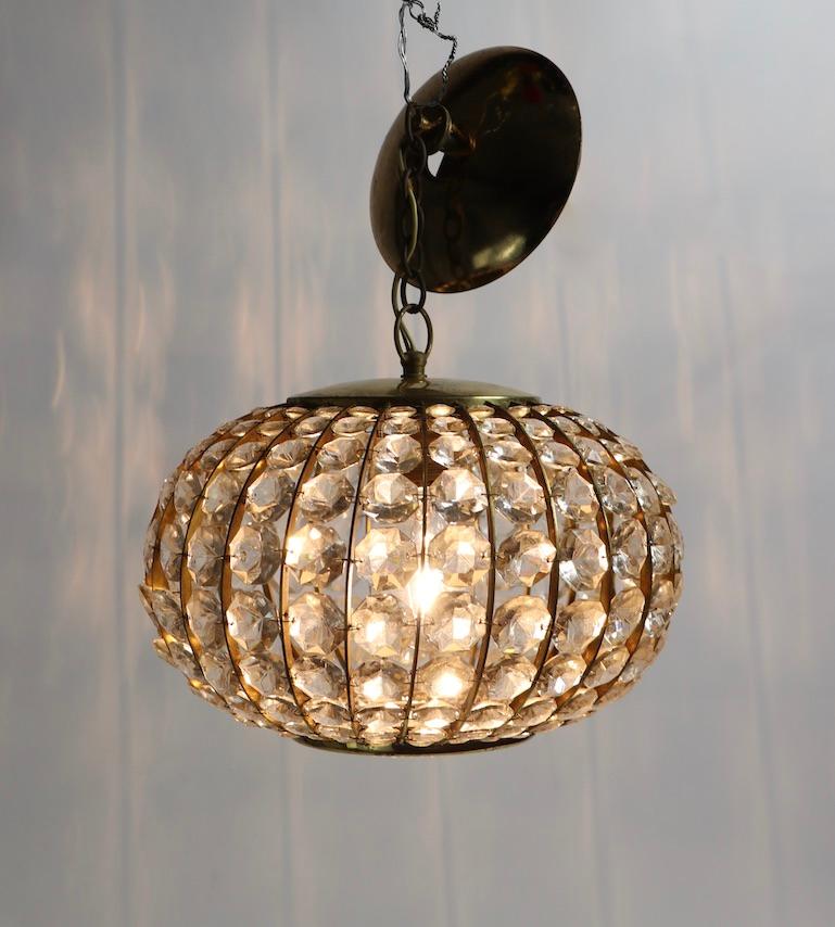 Stunning Austrian chandelier of faceted crystal on a brass frame structure. This example still retains the original glass disk diffuser on the bottom, which is usually missing in vintage examples. The fixture shows some cosmetic wear to the e