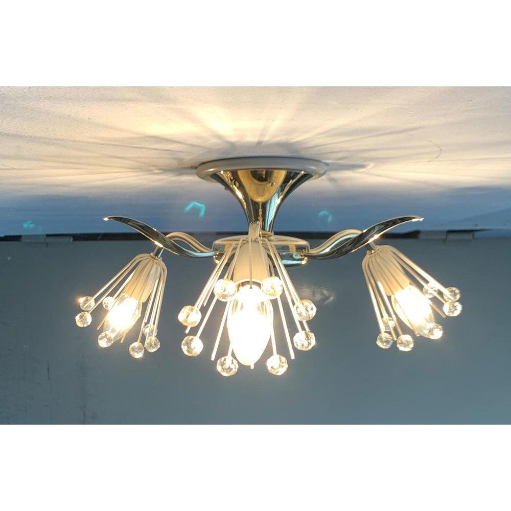 Raro lampadario da soffitto di Rupert Nikoll su disegno di Emil Stejnar.

Un design imponente le cui forme e dettagli si ispirano al mondo vegetale. I bracci di ottone curvi sono disposti radialmente intorno a un albero a forma di tromba. Tra questi