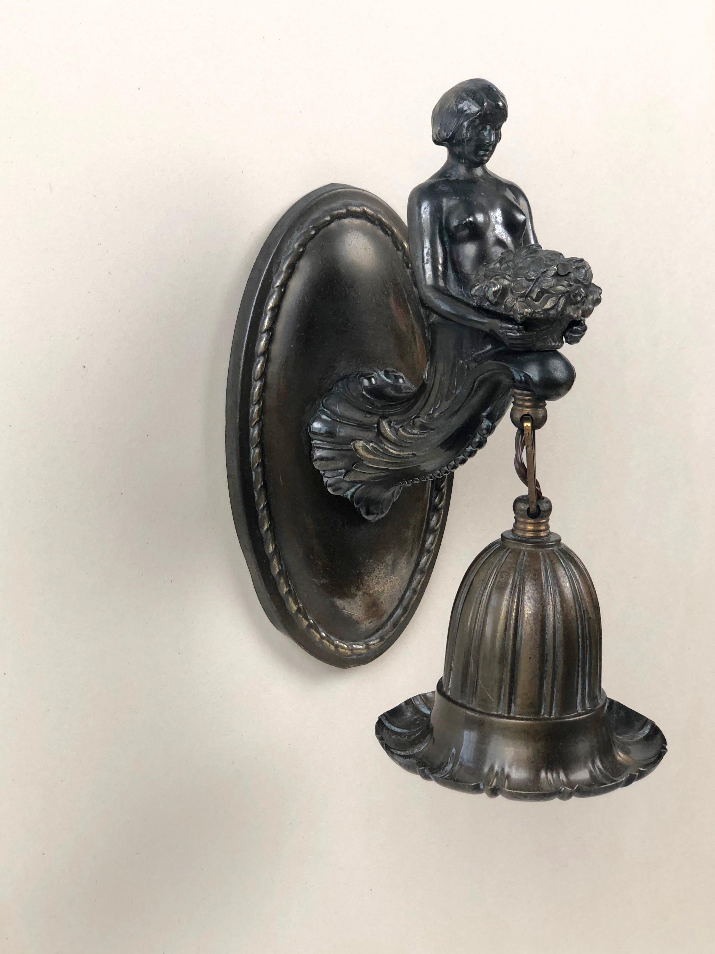 A delicate wall sconce, made in Austria. A medallion shaped wall bracket with a women attached to it, holding a bouquet of roses.
The fixture is mounted in flower shaped form and hangs under the flowers.