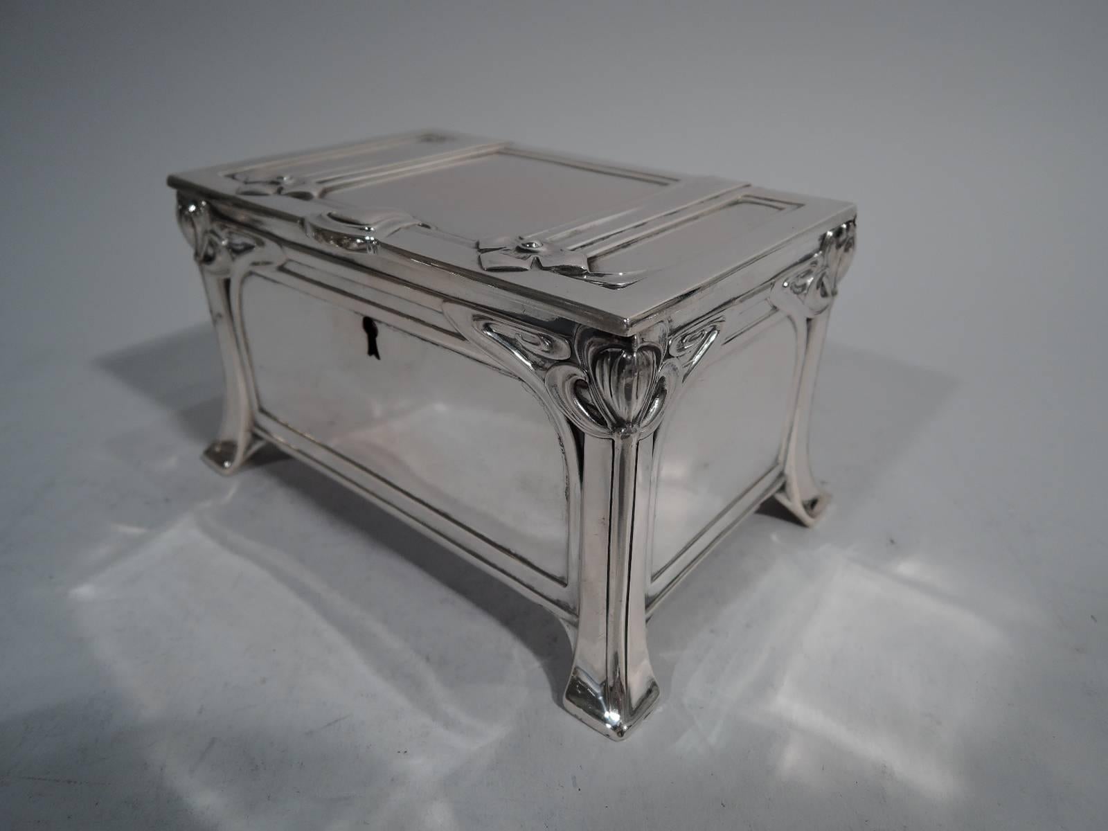 Austrian Jugendstil casket in 800 silver. Rectangular with straight sides, flat hinged cover, and splayed block supports. Sides and cover paneled. Ornament stylized and curvilinear. Sides have corner flowers between whiplash lines. Cover has straps