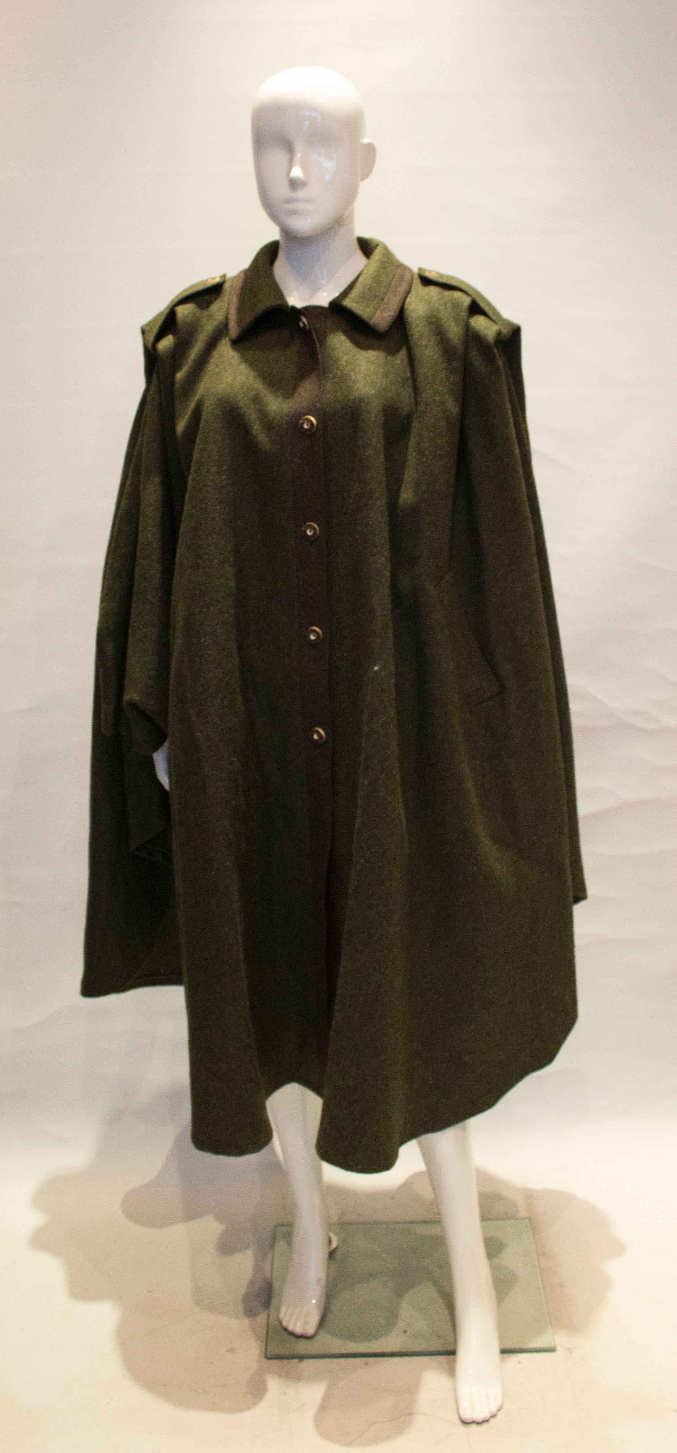 A chic and practical cape  in 100 % wool.  Made by  Salzburger Trachten , the cape is in a sage green colour, and has horn button from opening. It has arm holes created with detachable button fastenings and two pockets.  It has a two button detail