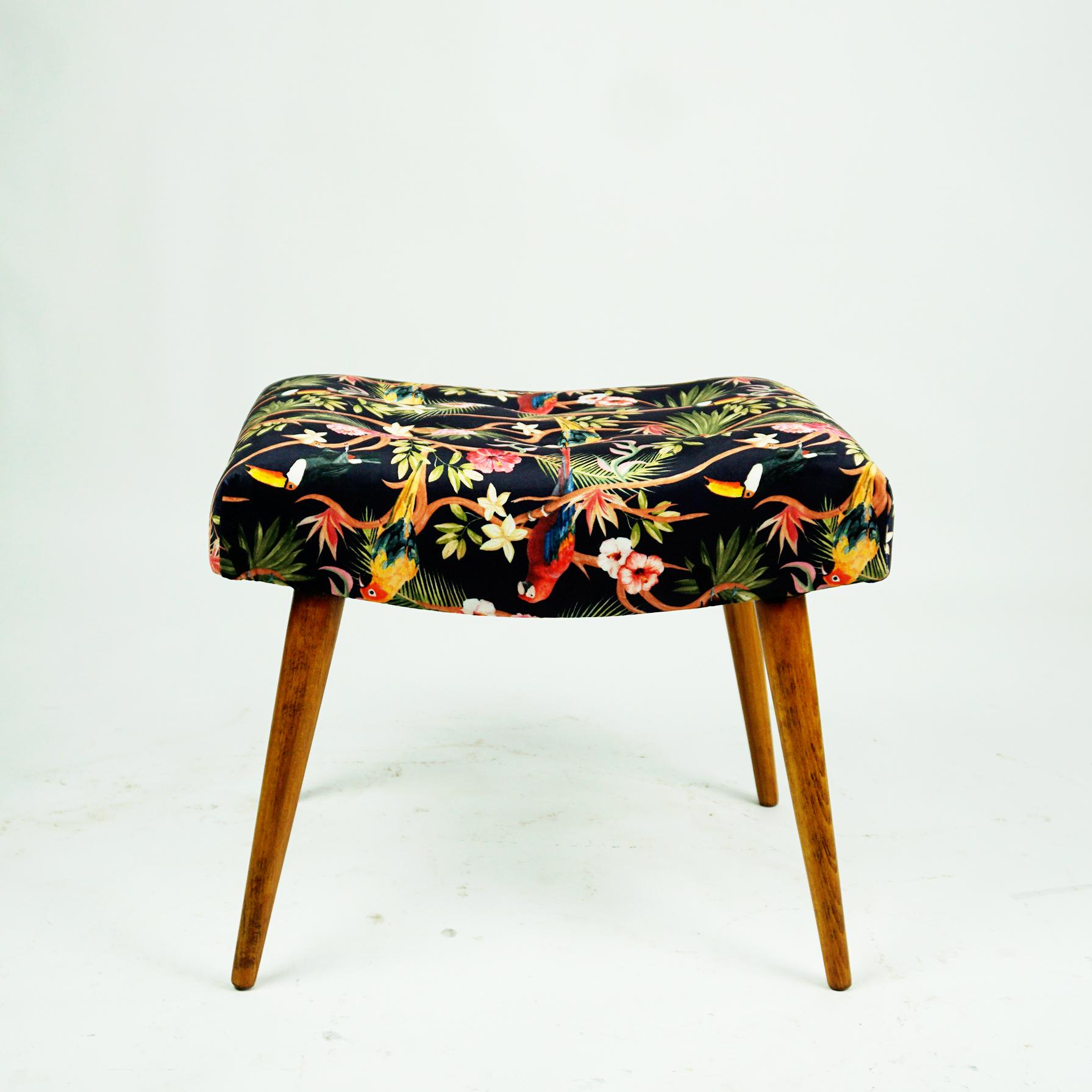 Offered is a charming Mid-Century Modern beechwood stool, ottoman or pouf that is newly upholstered in black and multicolored velvet with flowers and birds ornaments. It has slightly tapered steel legs and has been newly upholstered. It will be a