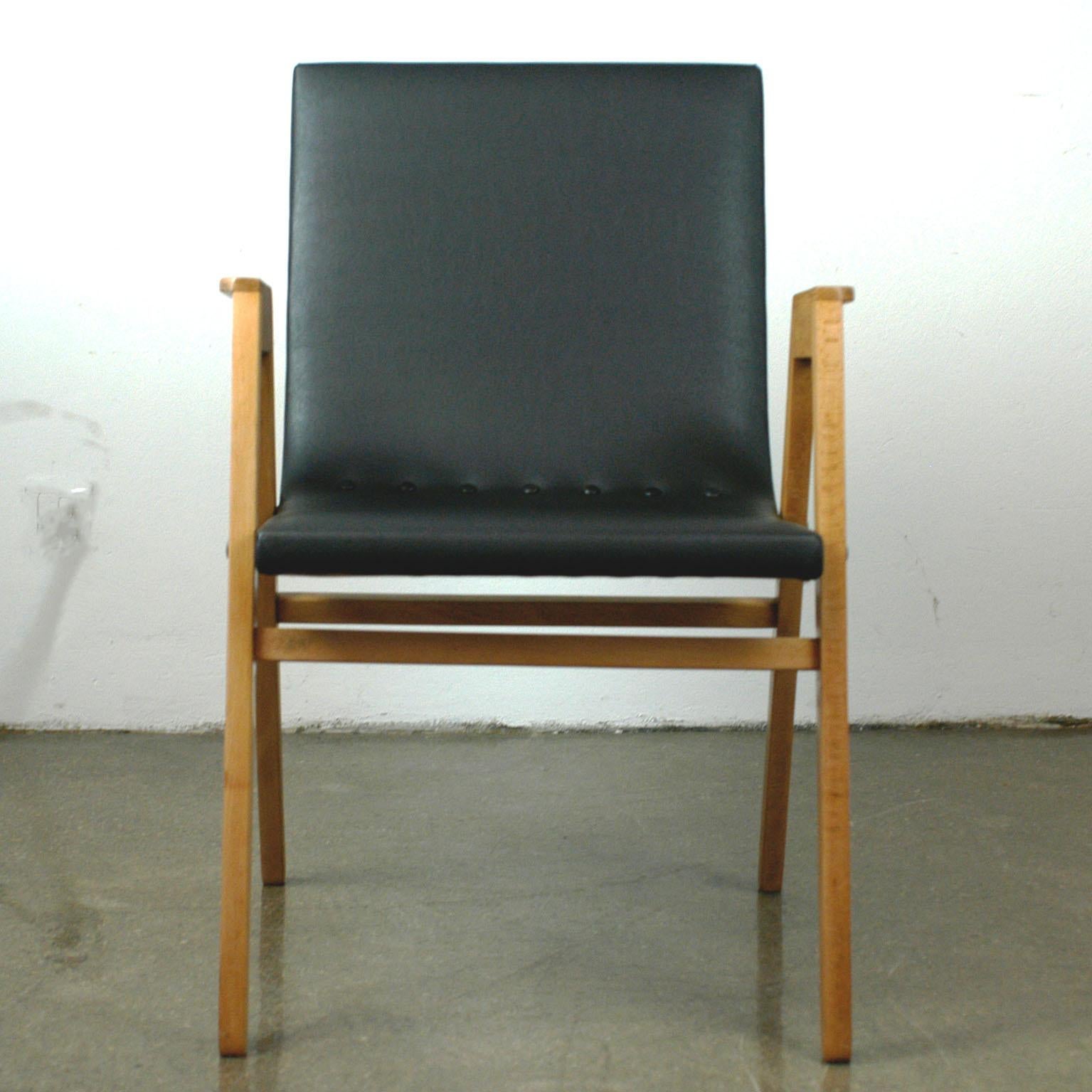 Sedia impilabile austriaca della metà del secolo scorso disegnata da Roland Rainer in eccellenti condizioni di restauro. Presenta una struttura in legno di faggio con schienale e seduta rivestiti in similpelle nera rinnovata e bottoni. Questa sedia
