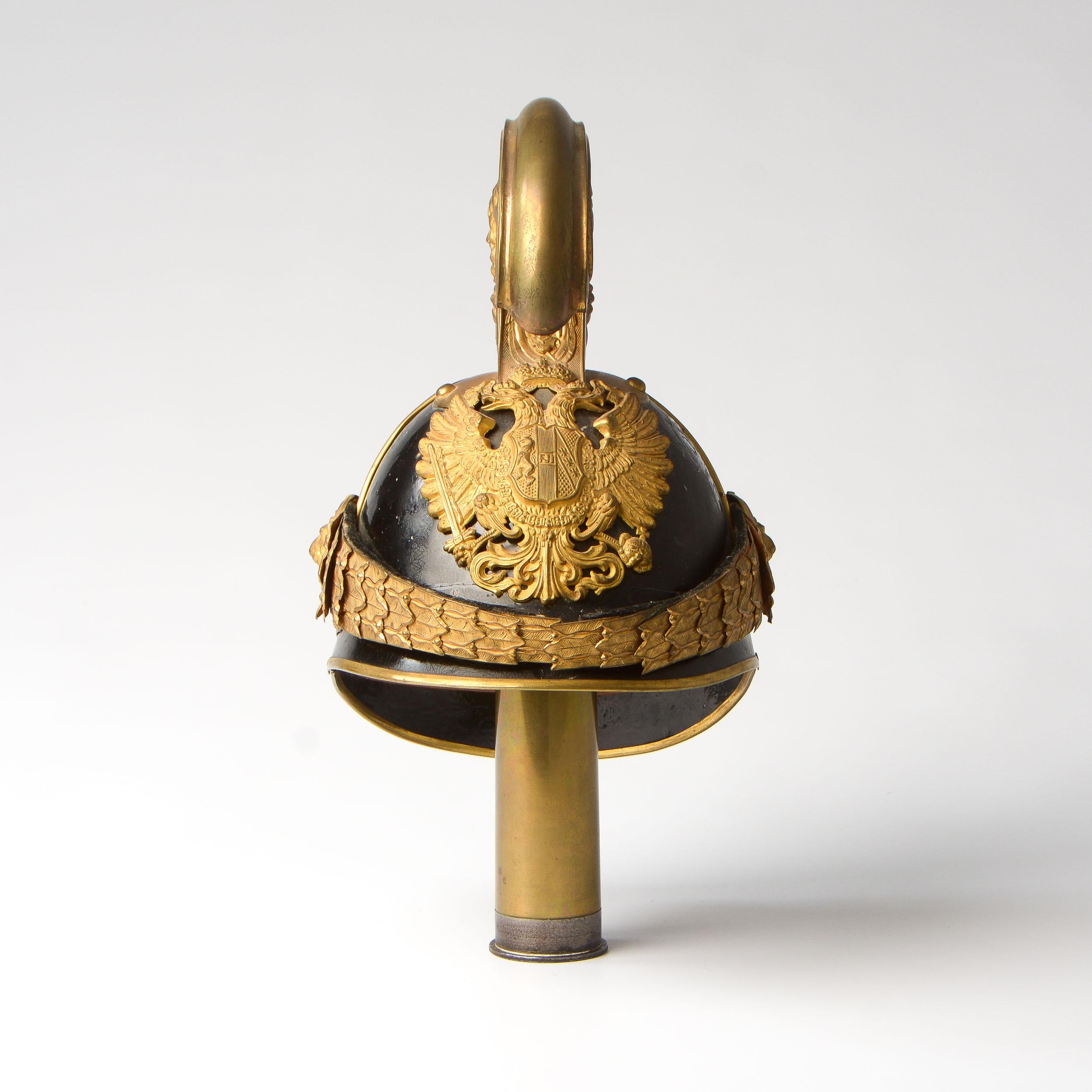 An original Austrian model 1905 Dragoon Officers’ helmet. Black enameled metal body with brass trim and high stamped-brass comb with a vignette of a lion in combat with a snake embossed on each side. Brass Austrian double-headed eagle front plate