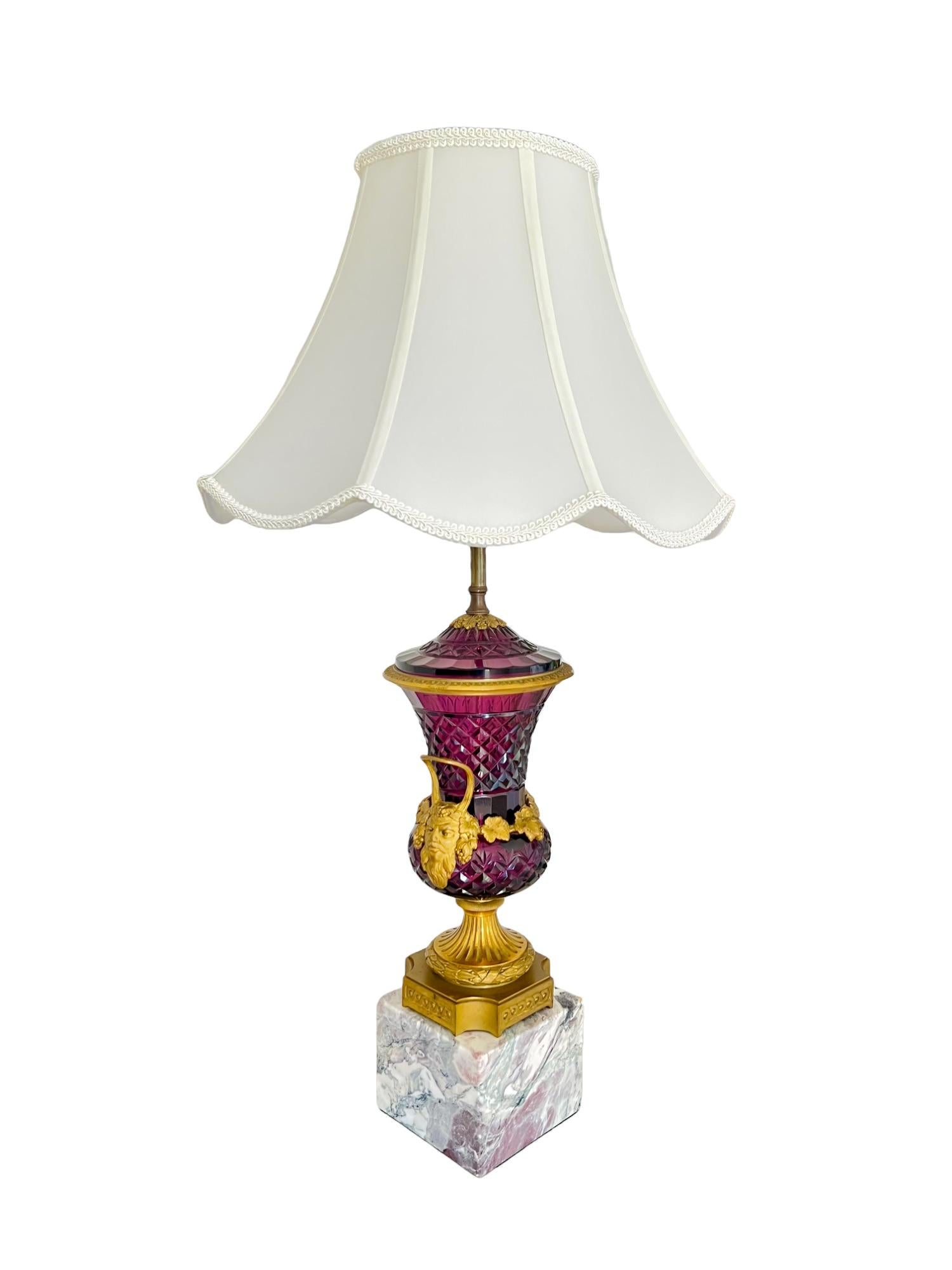 An antique late 19th century cut amethyst glass lidded campana urn vase from Austria, set atop a marble block and converted into a dual socket table lamp with pull cord operation. The stunning vase features diamond facets, a Bacchus themed motif