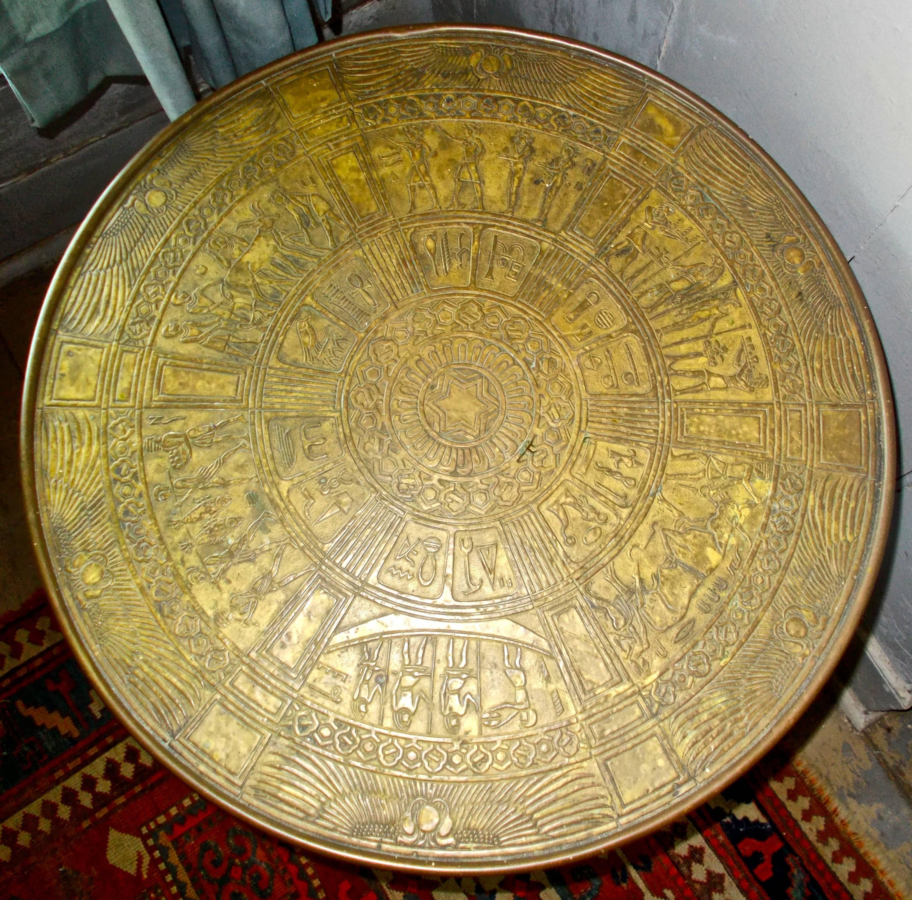 An Austrian secessionist table with Egyptian motifs. A circa 1890 round wooden table with ebonized legs and ball feet. Top and base surfaces covered with embossed brass sheet. Top is embossed with Egyptian designs and motifs. Some cracking to the