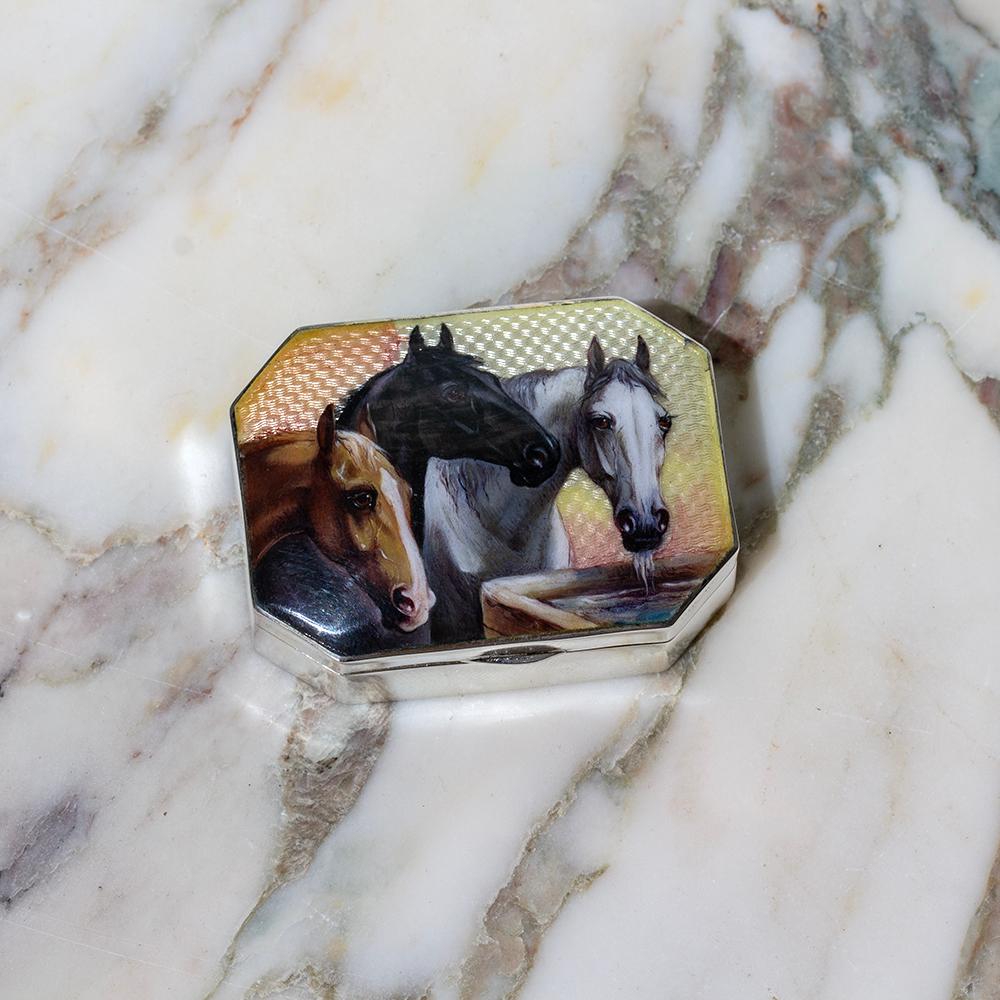The box of rectangular shape with faceted corners topped with an enamel scene featuring three horses grazing by the watering trough amongst a sunburst enamel background. The interior of the box is finished in Silver gilding and bares a thumb tab to