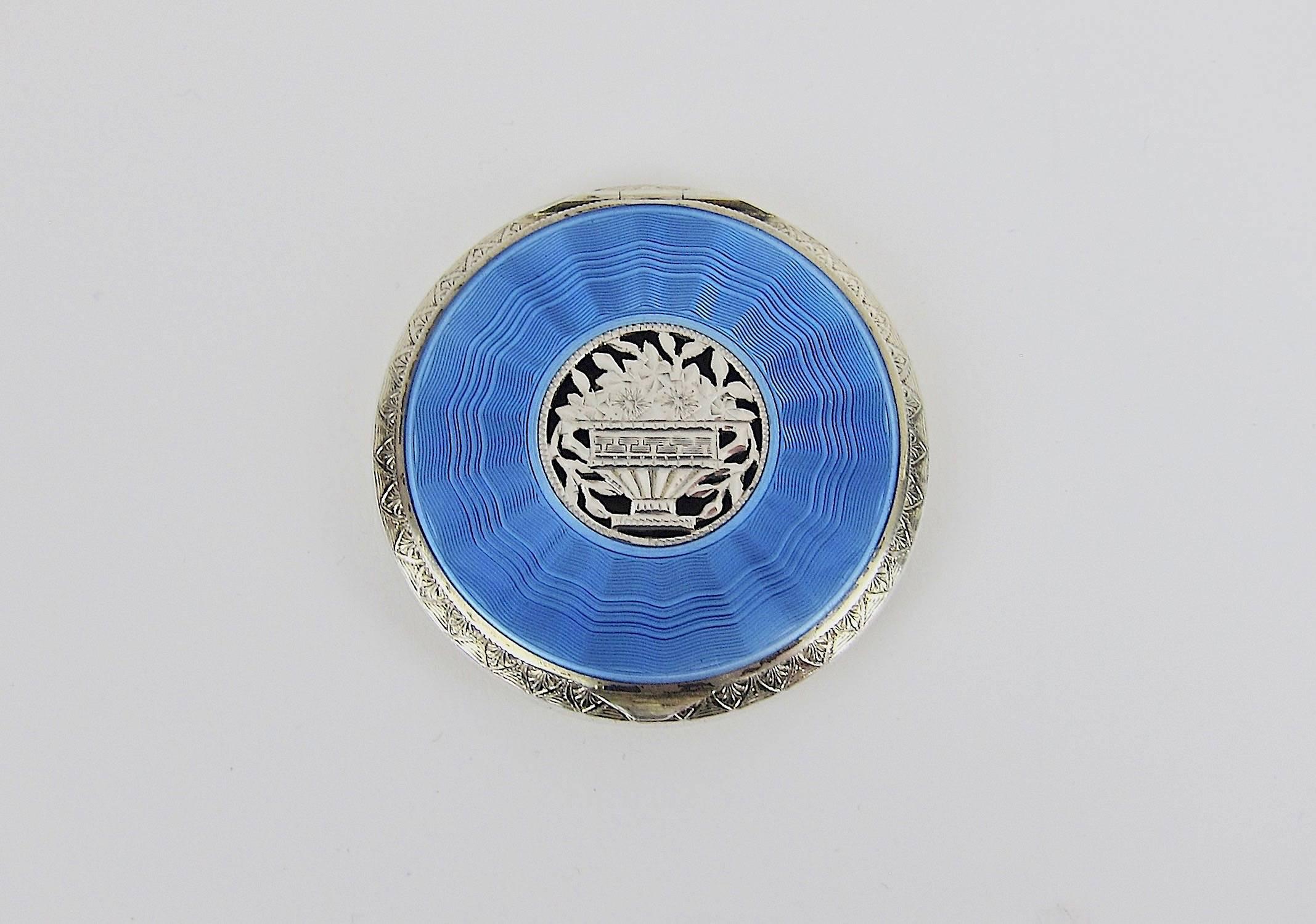 An antique sterling silver hinged compact from Austria with sky blue guilloche enamel decoration. This early 20th century accessory is decorated with a wide band of blue enamel encircling an engraved openwork central floral design. The compact opens