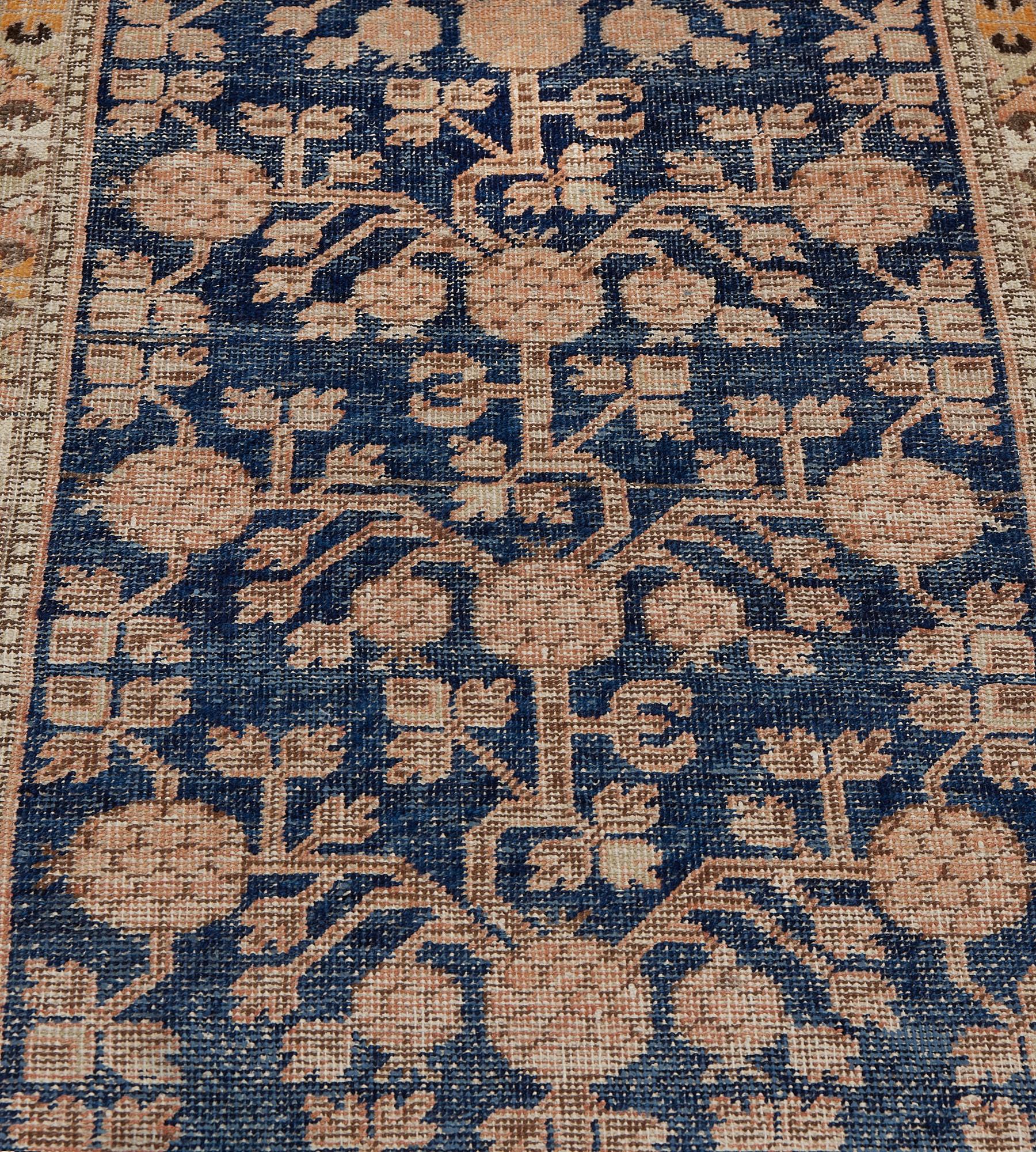 Este antiguo camino de mesa Khotan, de hacia 1890, presenta un campo azul real sombreado con un diseño general de granadas y frondosas enredaderas de color marfil y terracota suave, en un borde marrón topo de enredaderas florales policromadas con