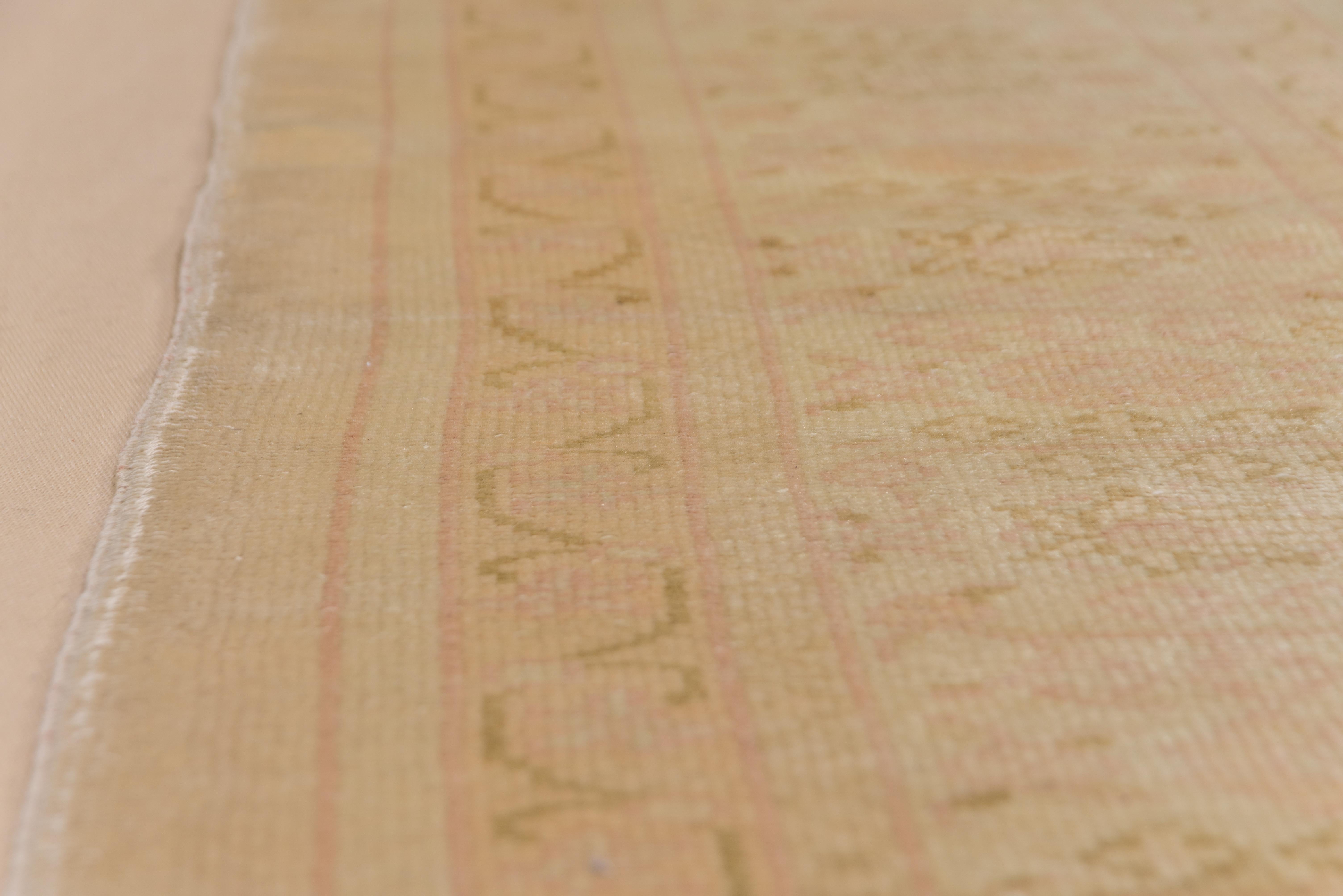 Dieser mittelgrobe Teppich aus einer westanatolischen Werkstatt zeigt ein hellbraunes, umlaufendes Muster auf einem Grund aus Sand-Eierschalen. Cremefarbene Bordüre mit hellen rostfarbenen Palmetten und geraden Blumenspritzern. Grob gewebt.