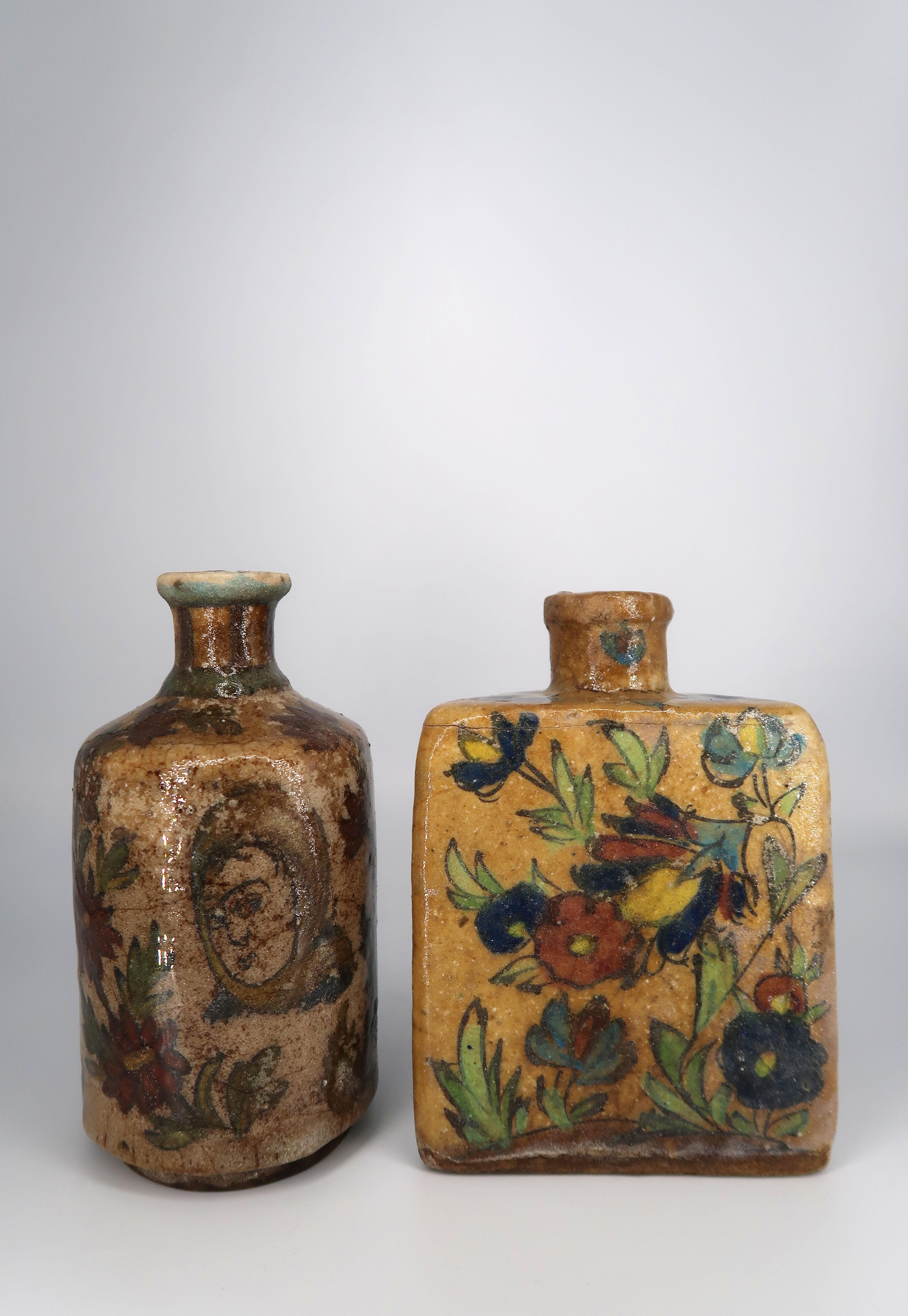 Two magnificent Middle Eastern antique handmade ceramic tea bottles with hand painted highly colorful decor and clear glaze. One round flask, one triangular. Dark and light blue, burgundy, yellow, green and red floral decorations with a female